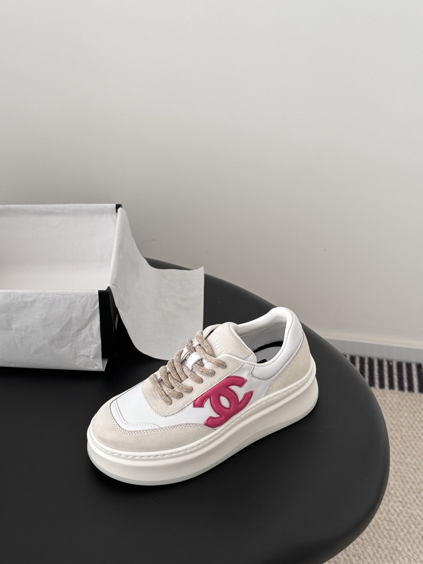 Pair of Chanel white and beige platform sneakers with pink CC logo next to a black Chanel shoe box - Hình 6