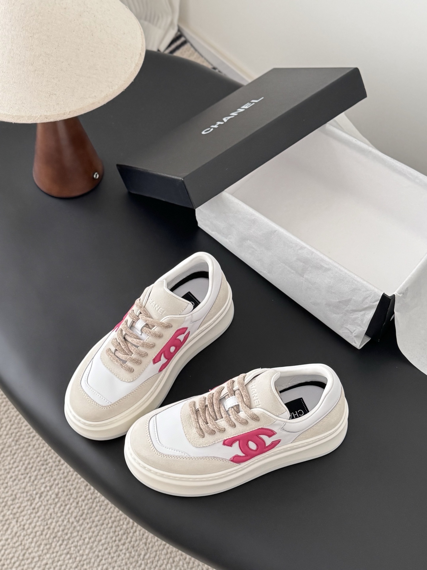 Pair of Chanel white and beige platform sneakers with pink CC logo next to a black Chanel shoe box - Hình 5