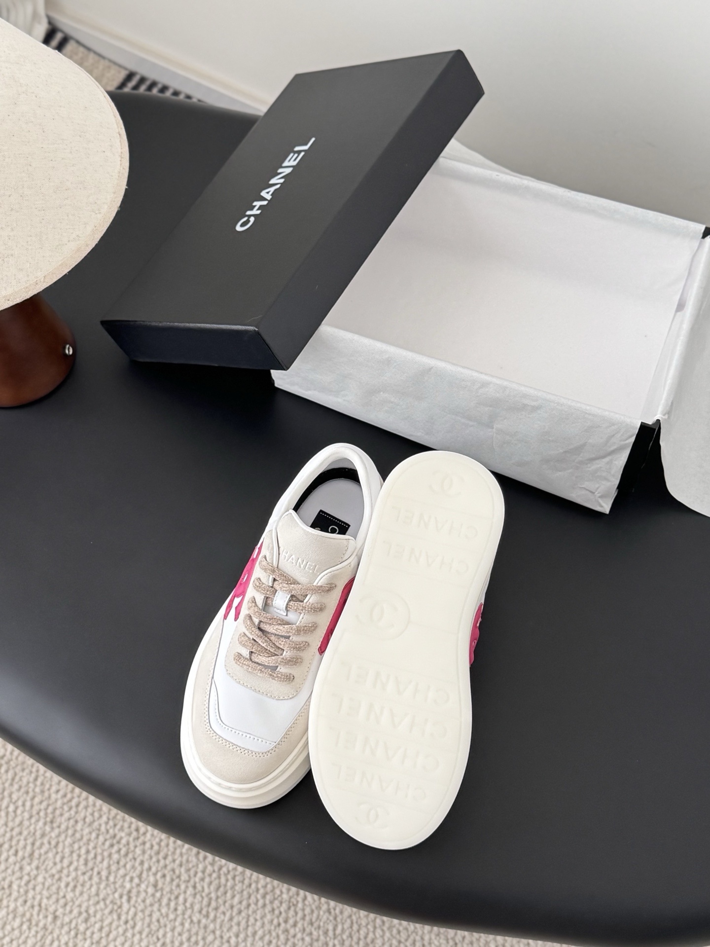 Pair of Chanel white and beige platform sneakers with pink CC logo next to a black Chanel shoe box - Hình 4
