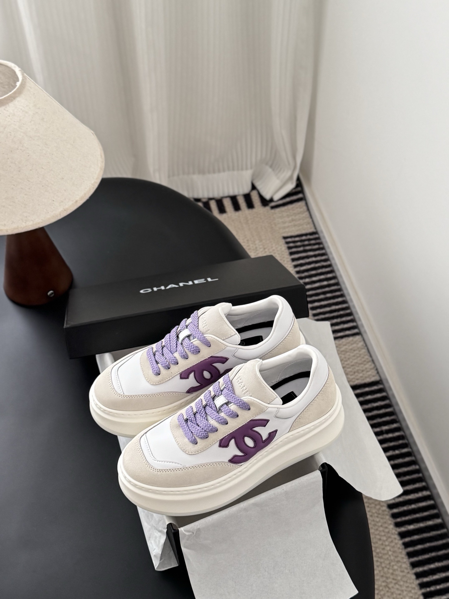 Pair of Chanel low-top platform sneakers in white leather and cream suede with purple CC logo and purple laces next to a black Chanel box. - Hình 9