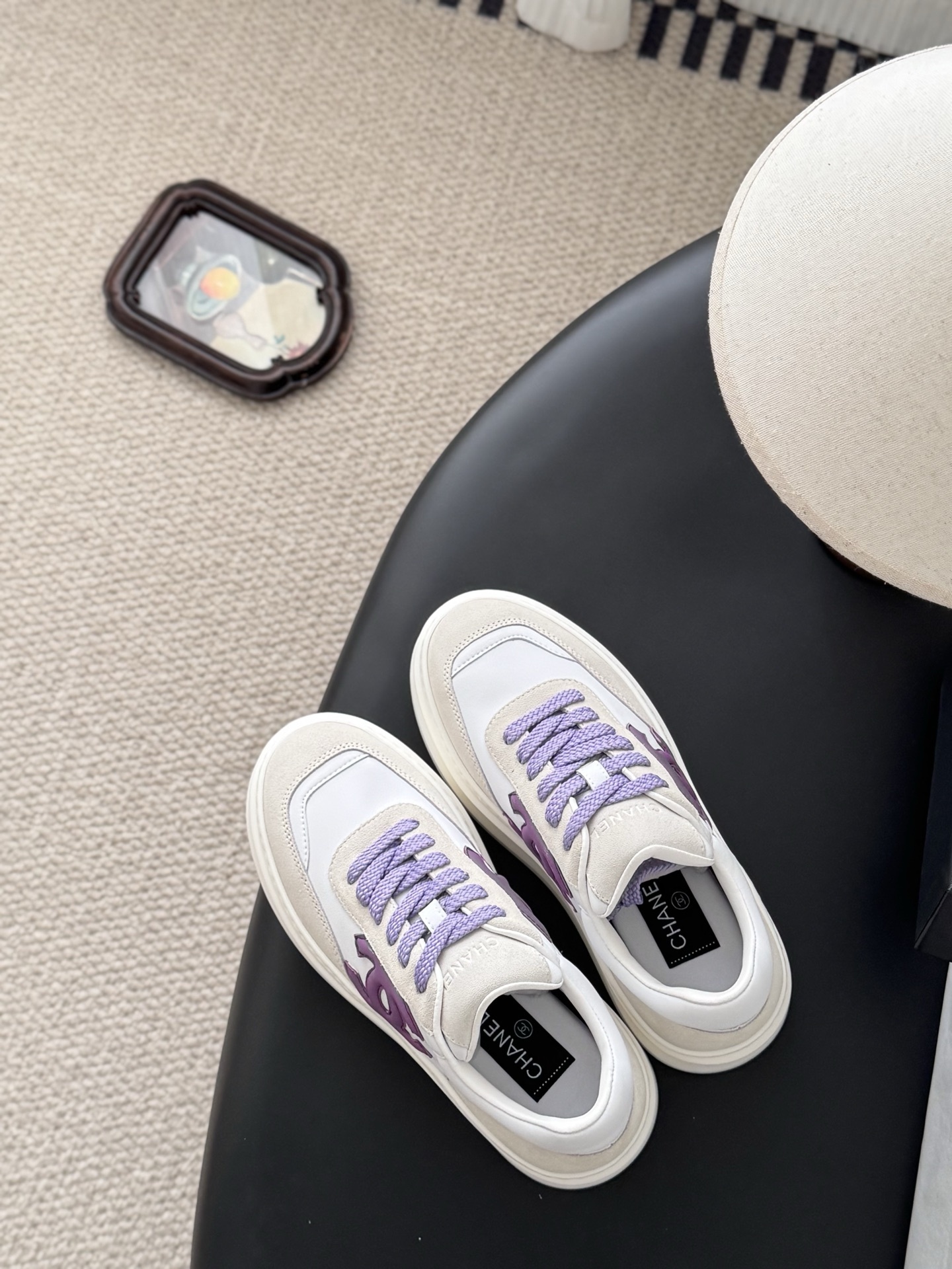 Pair of Chanel low-top platform sneakers in white leather and cream suede with purple CC logo and purple laces next to a black Chanel box. - Hình 8