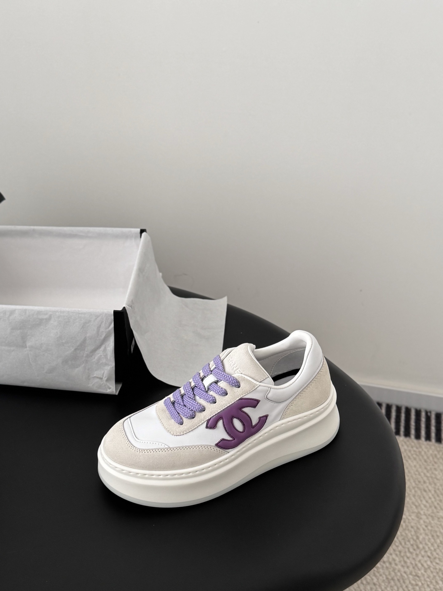 Pair of Chanel low-top platform sneakers in white leather and cream suede with purple CC logo and purple laces next to a black Chanel box. - Hình 6