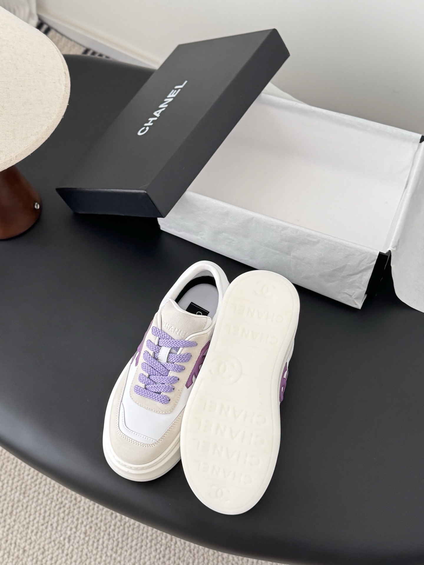 Pair of Chanel low-top platform sneakers in white leather and cream suede with purple CC logo and purple laces next to a black Chanel box. - Hình 4
