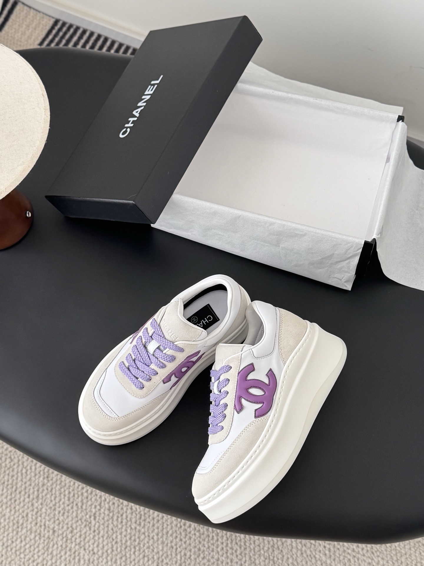 Pair of Chanel low-top platform sneakers in white leather and cream suede with purple CC logo and purple laces next to a black Chanel box. - Hình 3