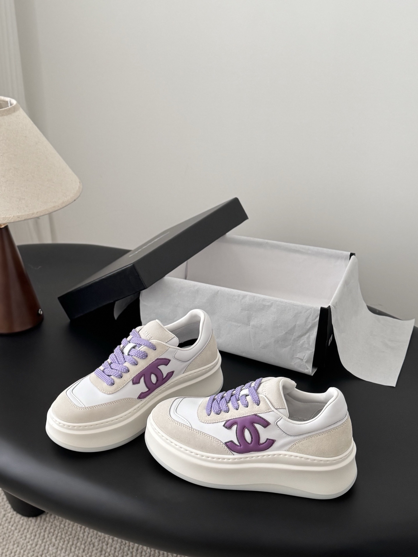 Pair of Chanel low-top platform sneakers in white leather and cream suede with purple CC logo and purple laces next to a black Chanel box. - Hình 2