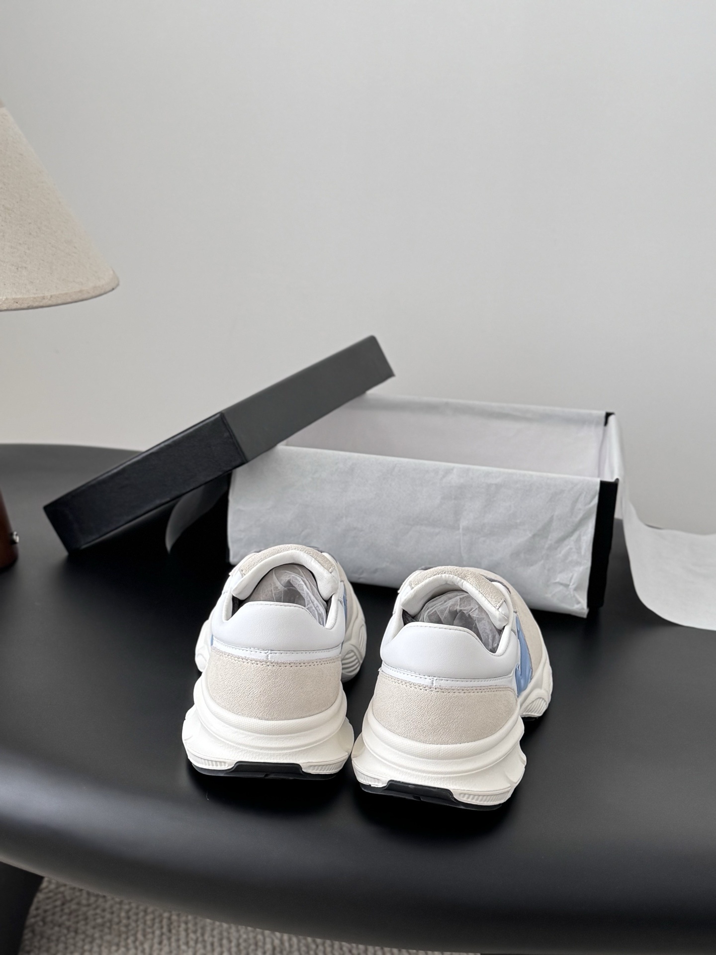 A pair of Chanel sneakers in white and beige suede with a light blue CC logo and grey laces, shown with a black Chanel shoebox. - Hình 7