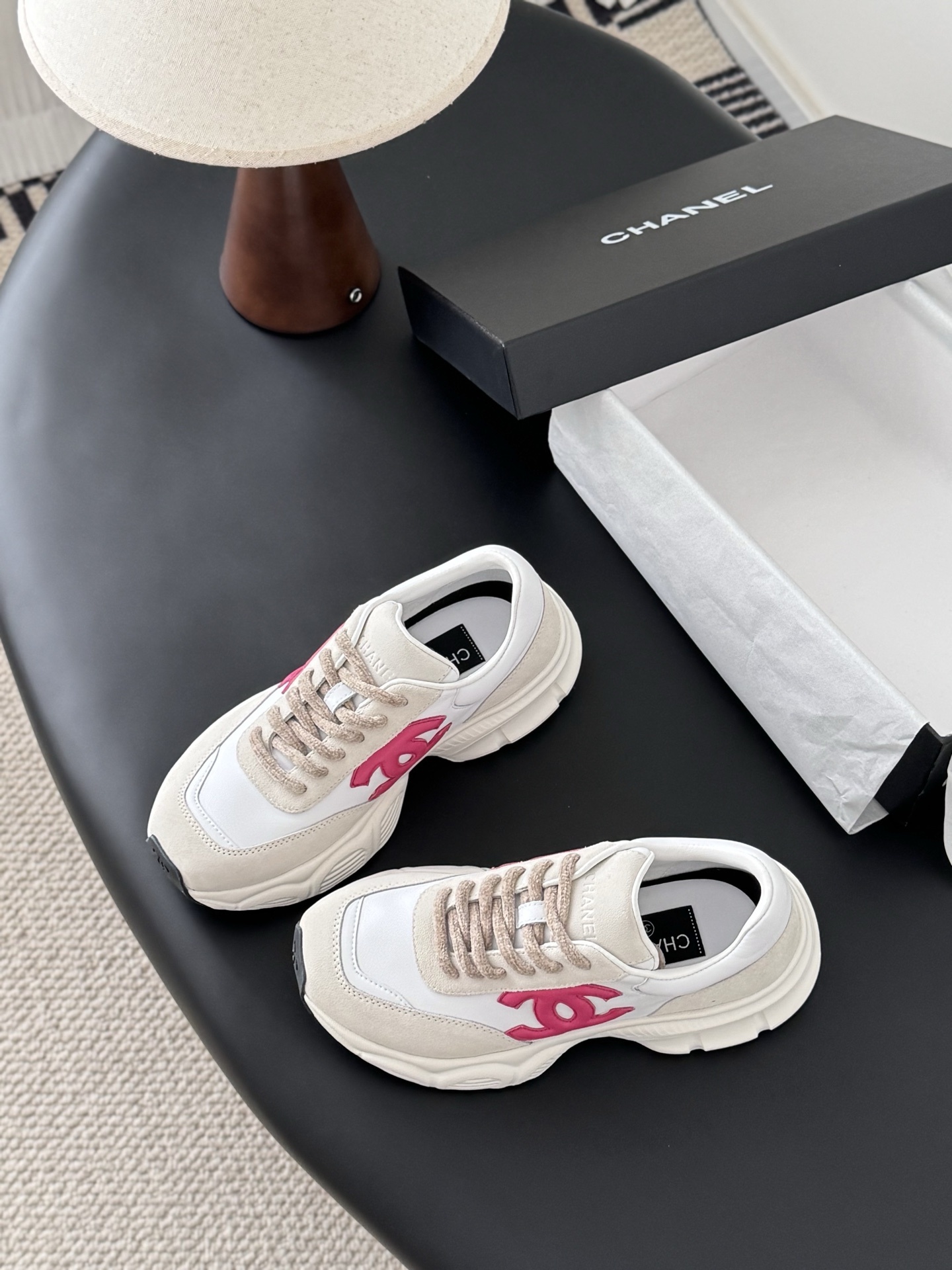 Pair of Chanel white leather and suede sneakers with pink interlocking CC logos next to a black Chanel box - Hình 6