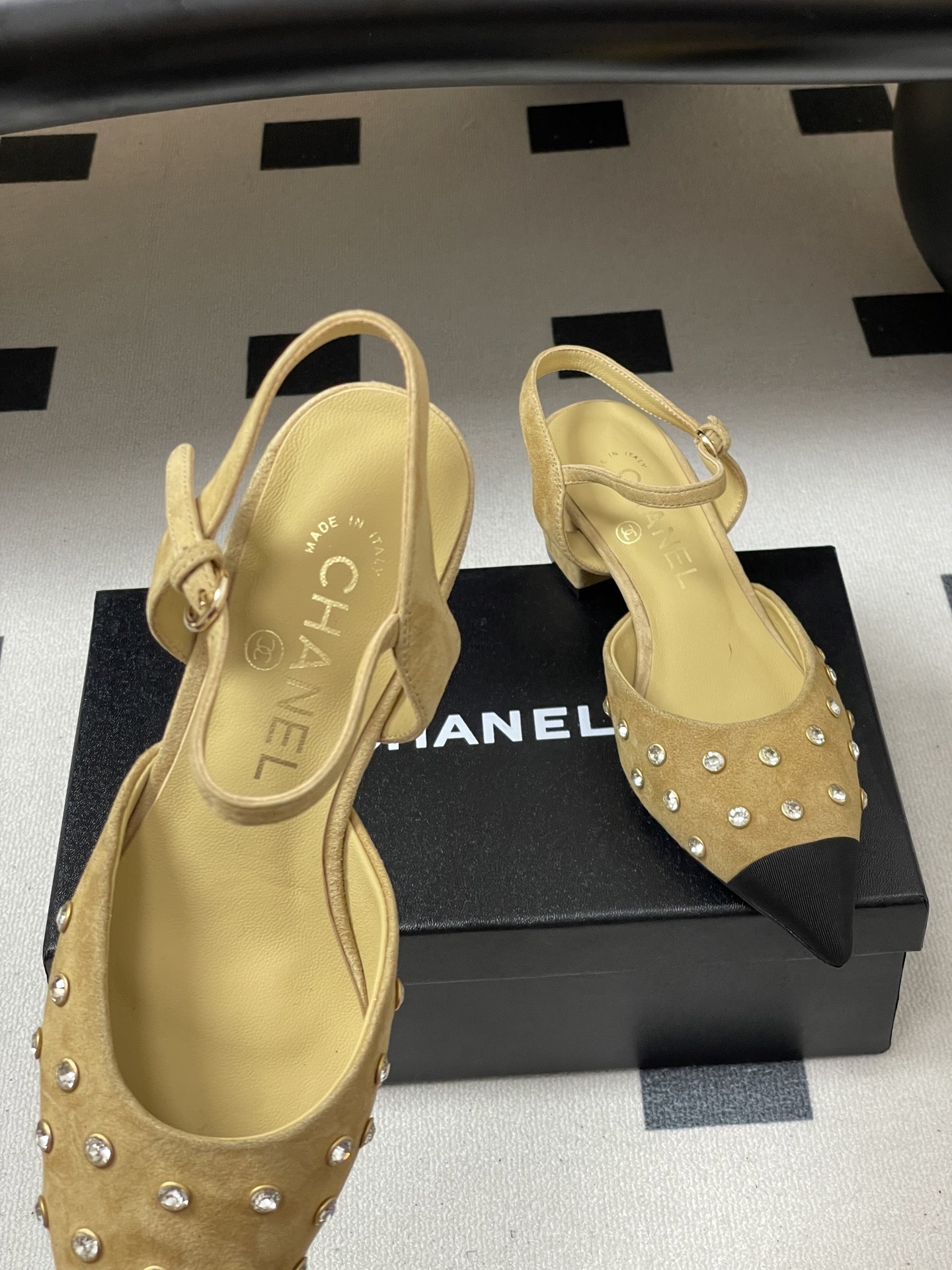 Pair of Chanel beige suede slingback pumps with black cap toes and crystal studs on a black surface - Hình 6