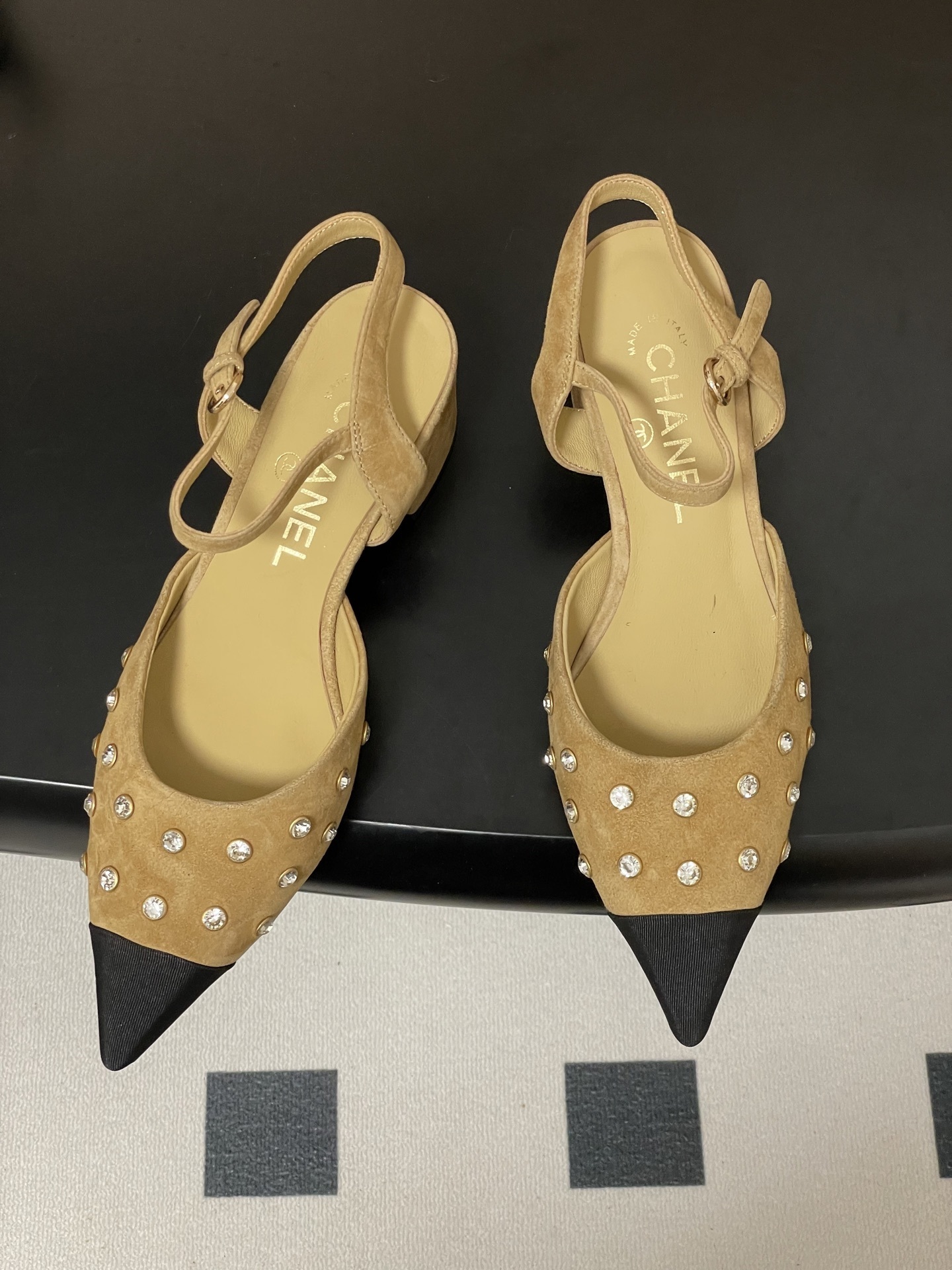 Pair of Chanel beige suede slingback pumps with black cap toes and crystal studs on a black surface - Hình 2