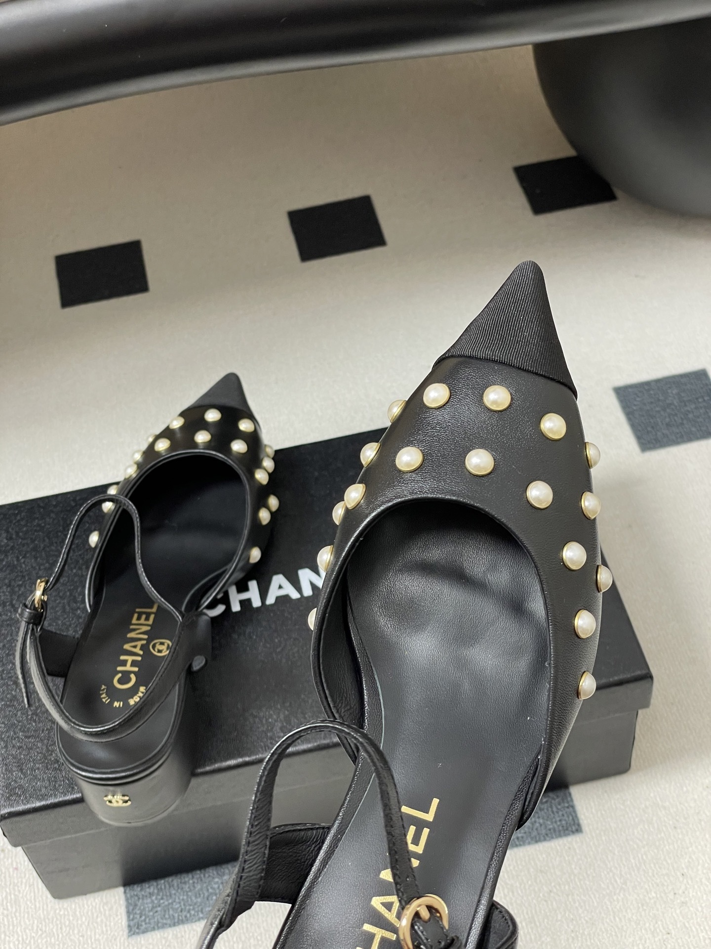 A pair of Chanel black leather slingback pumps with pearl studs and block heels displayed on a black surface. - Hình 9