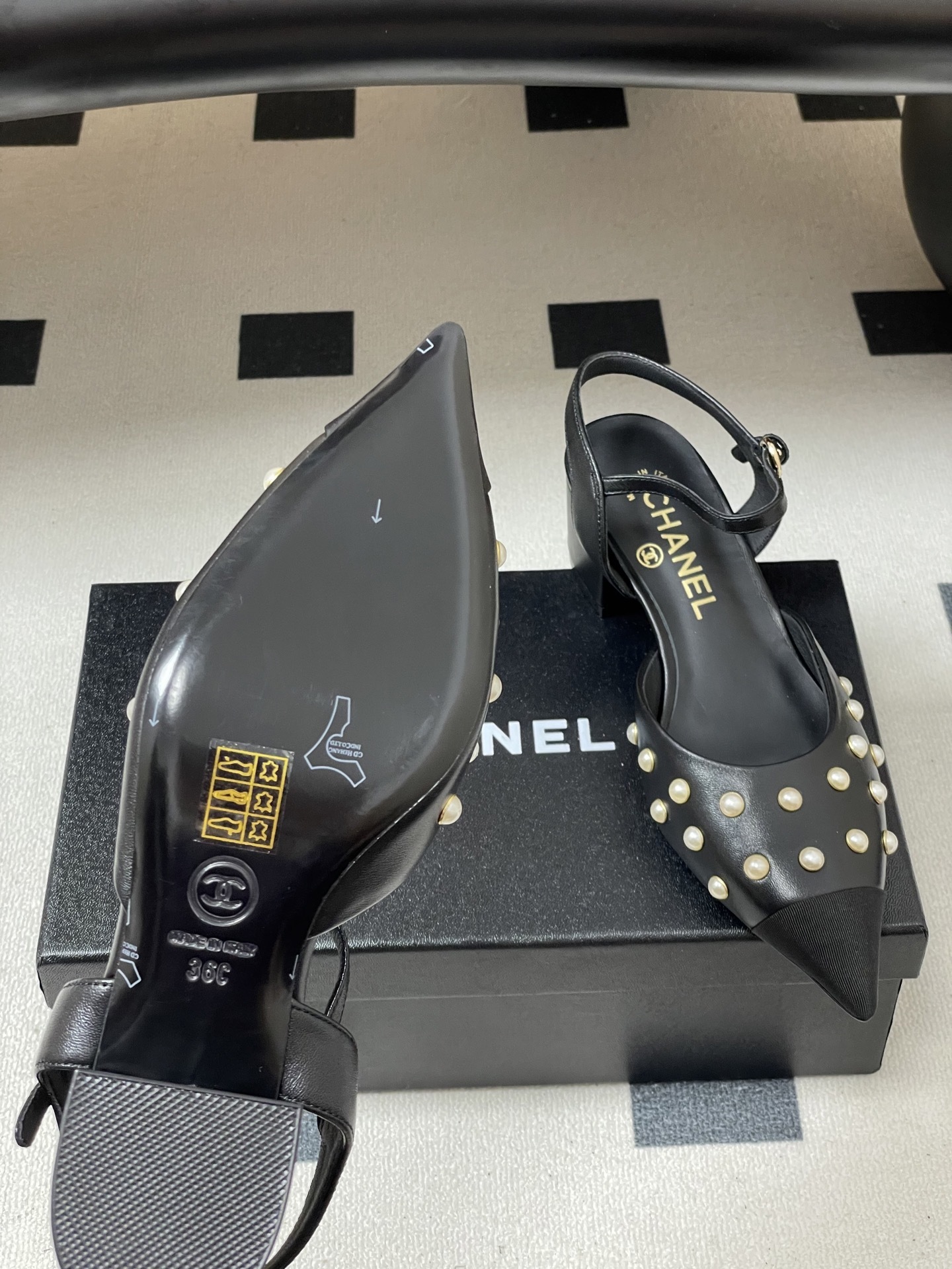 A pair of Chanel black leather slingback pumps with pearl studs and block heels displayed on a black surface. - Hình 8