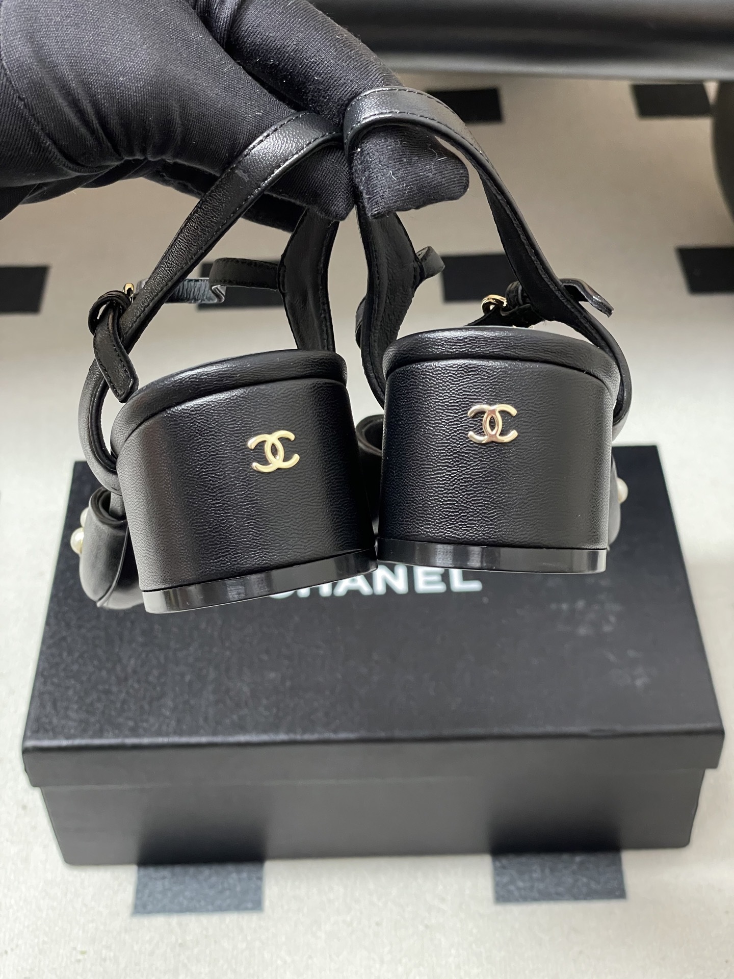 A pair of Chanel black leather slingback pumps with pearl studs and block heels displayed on a black surface. - Hình 7