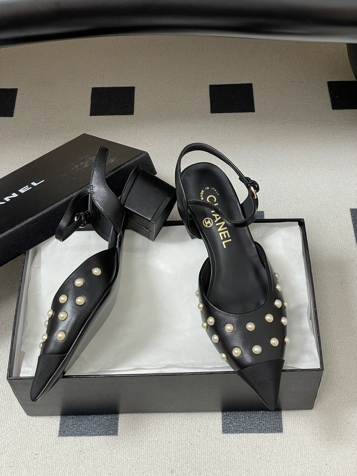 A pair of Chanel black leather slingback pumps with pearl studs and block heels displayed on a black surface. - Hình 6