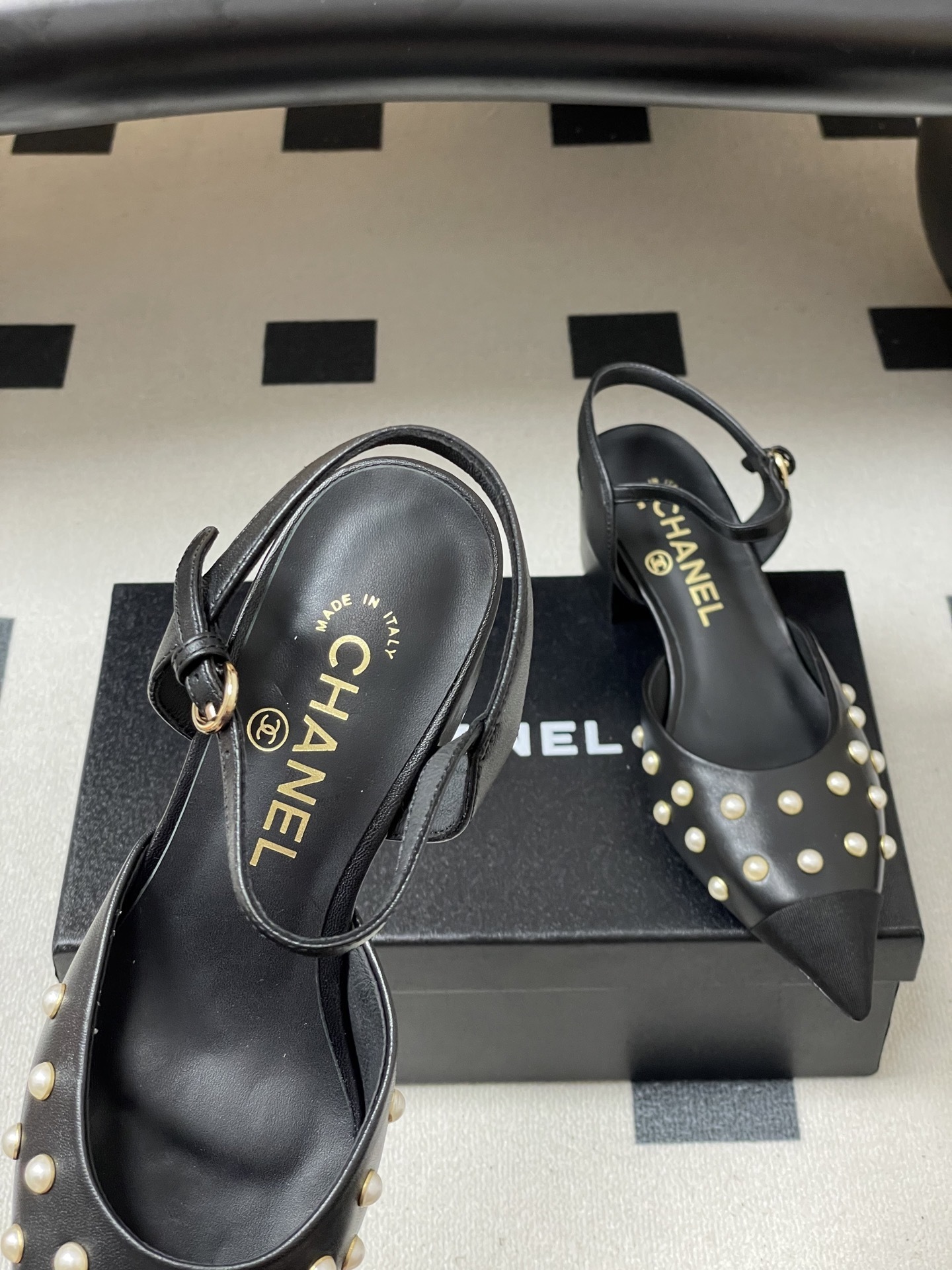 A pair of Chanel black leather slingback pumps with pearl studs and block heels displayed on a black surface. - Hình 5