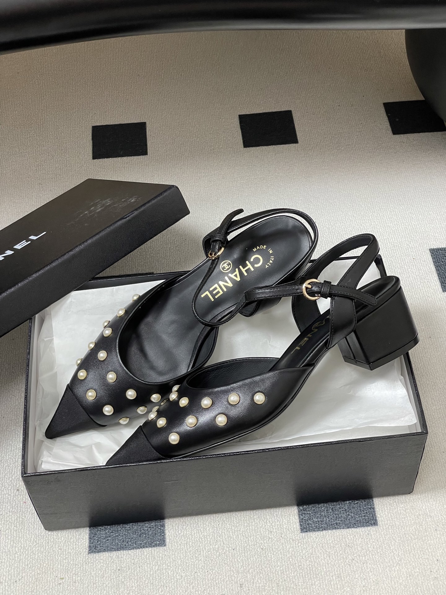 A pair of Chanel black leather slingback pumps with pearl studs and block heels displayed on a black surface. - Hình 4