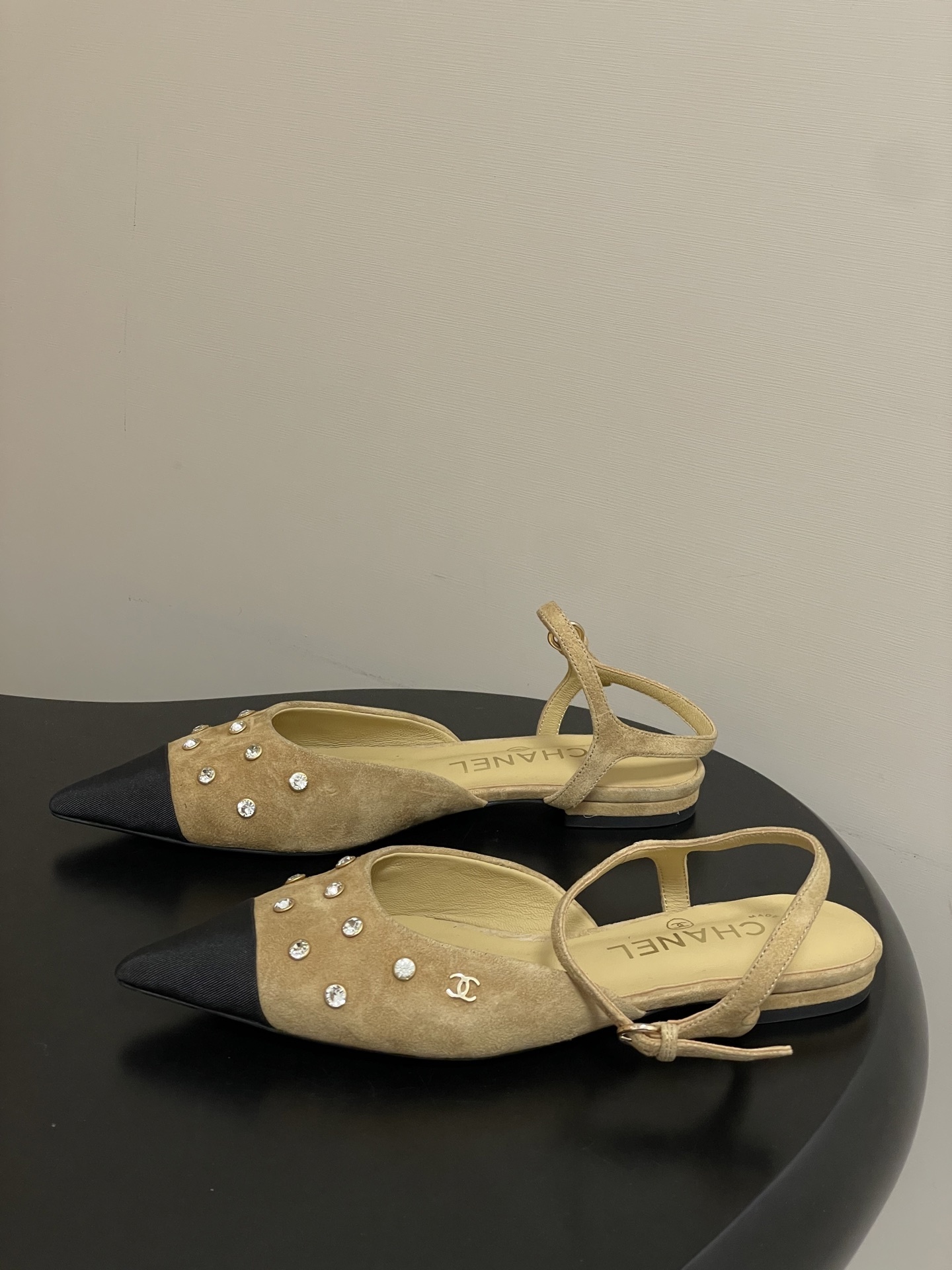 Luxury Chanel slingback flats in beige suede with crystal accents and black pointed toes on a black table. - Hình 3