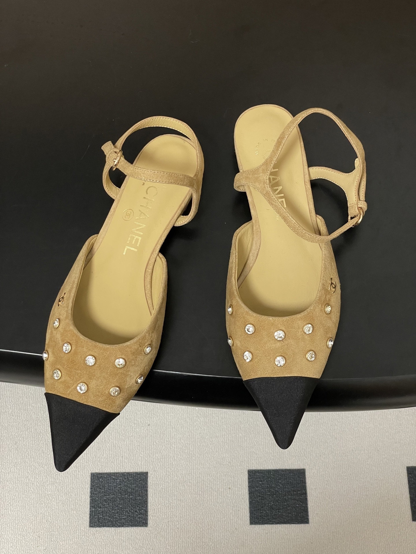 Luxury Chanel slingback flats in beige suede with crystal accents and black pointed toes on a black table. - Hình 2