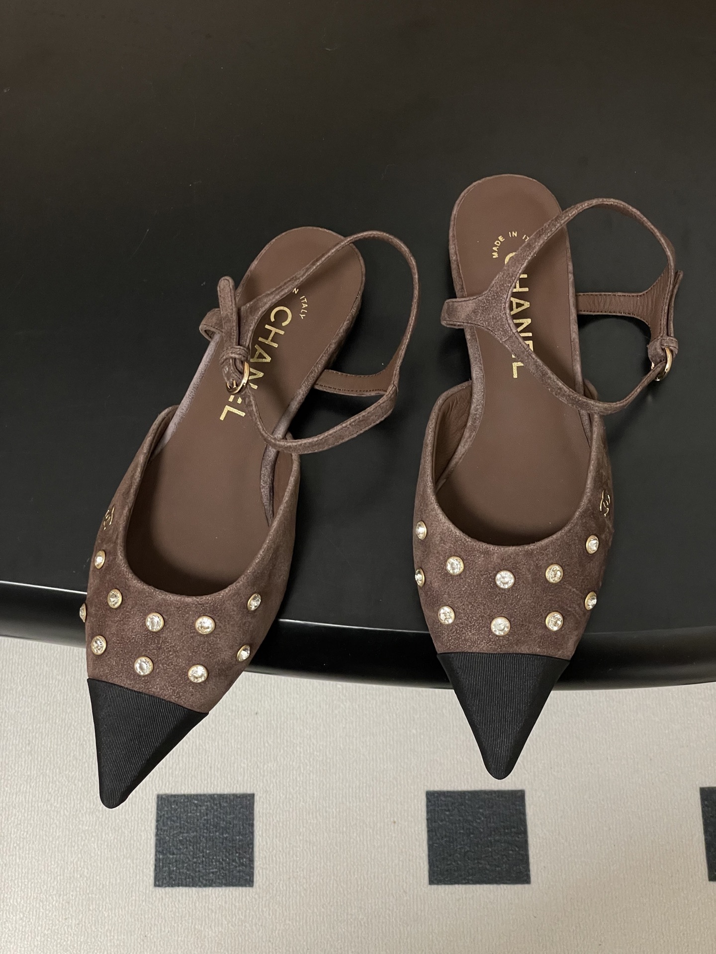 Pair of Chanel brown suede slingback flats with black pointed toes and crystal embellishments on a black table. - Hình 2