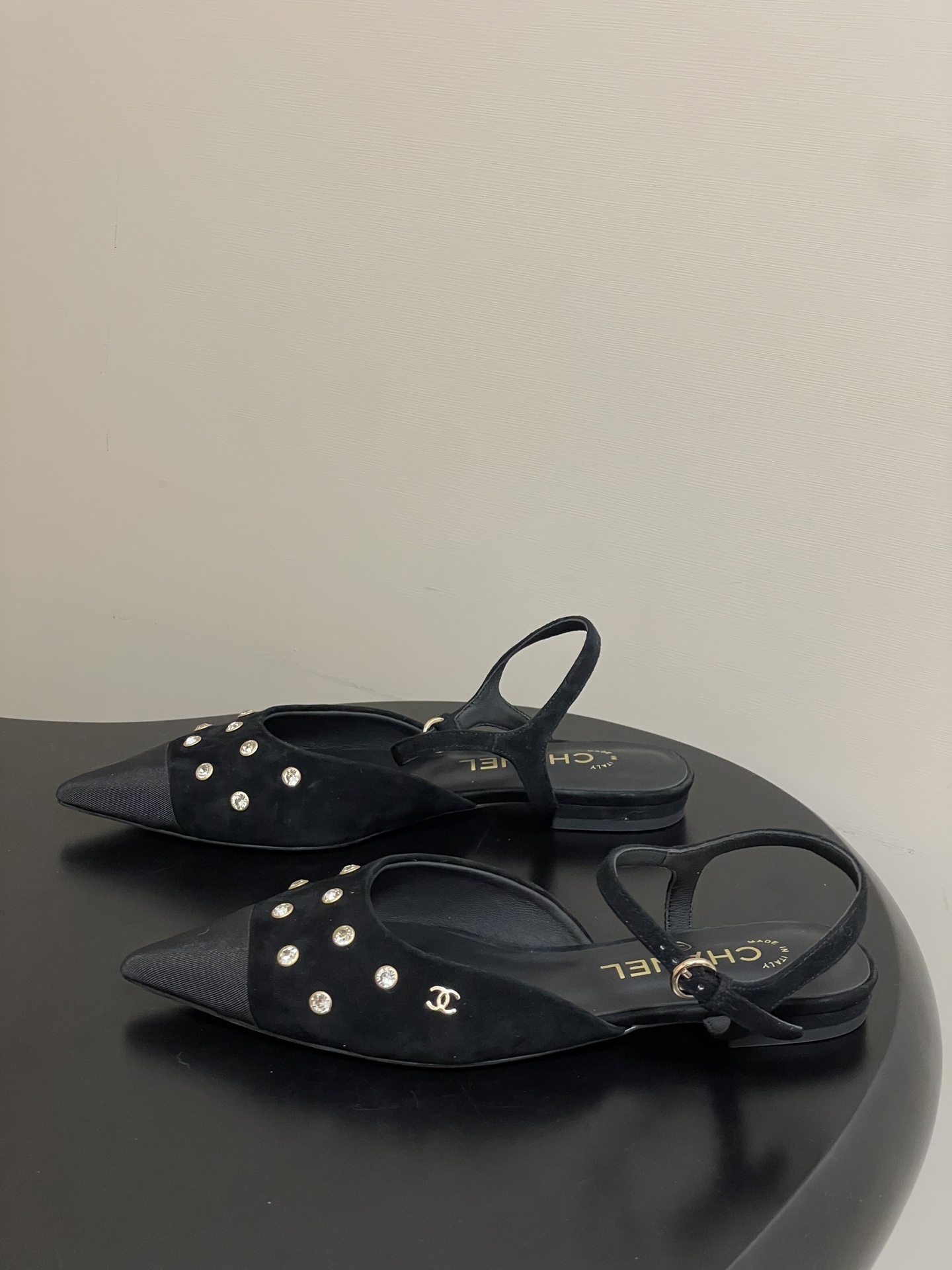 Chanel black suede pointed-toe slingback flats with crystal embellishments and gold CC logo on a black surface - Hình 3