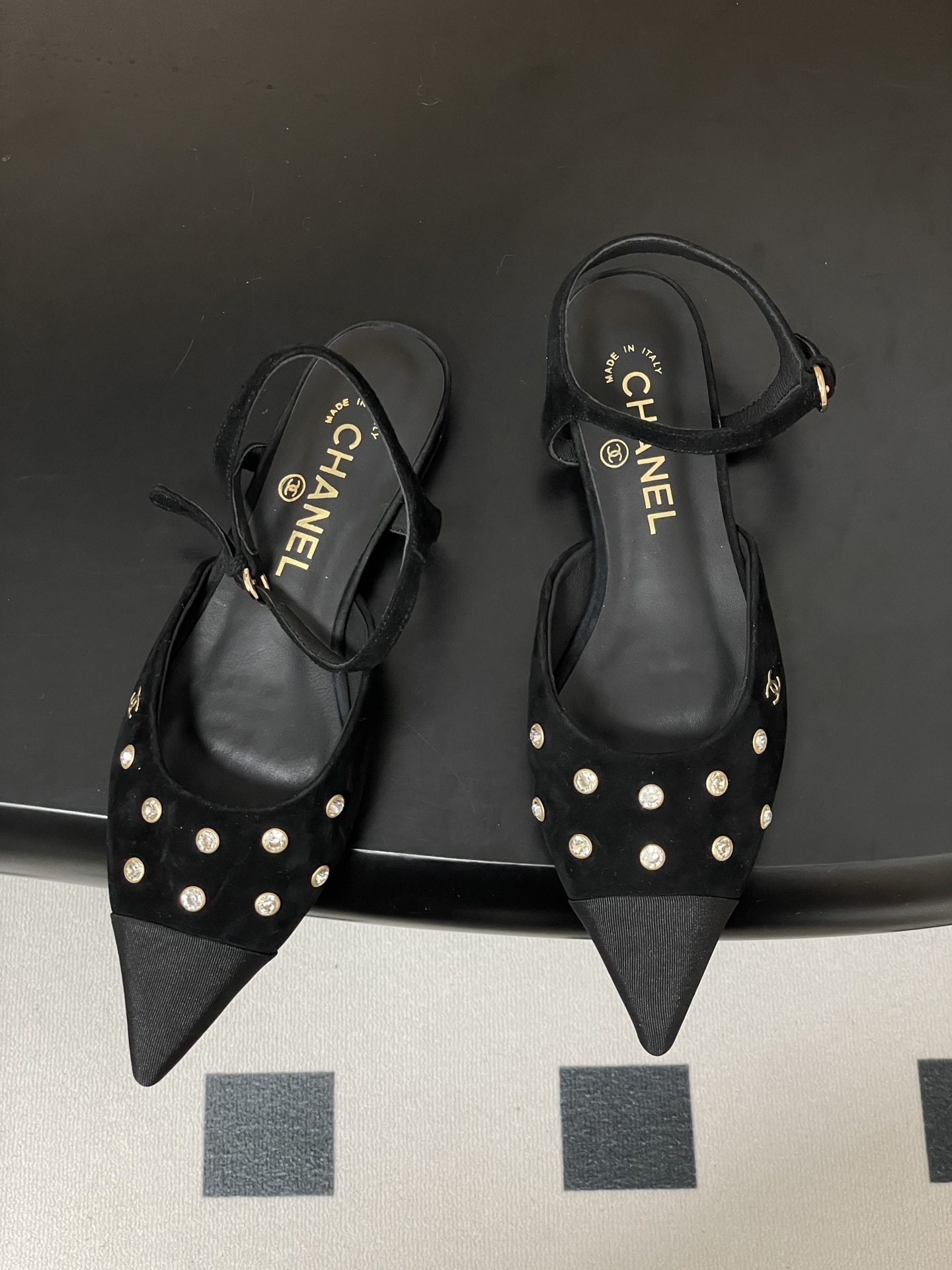Chanel black suede pointed-toe slingback flats with crystal embellishments and gold CC logo on a black surface - Hình 2