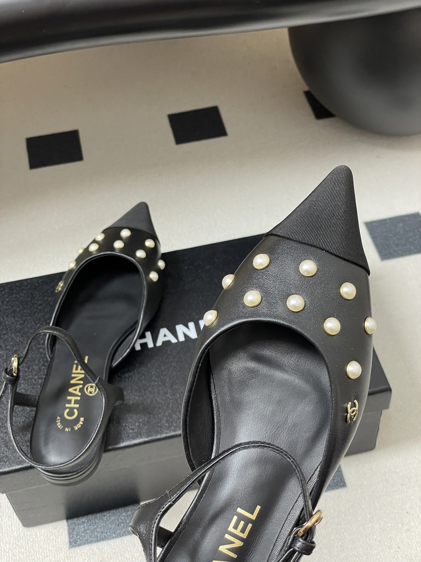 A pair of black Chanel slingback flats with pearl studs, pointed fabric cap toes, and gold CC logo on a black surface. - Hình 9