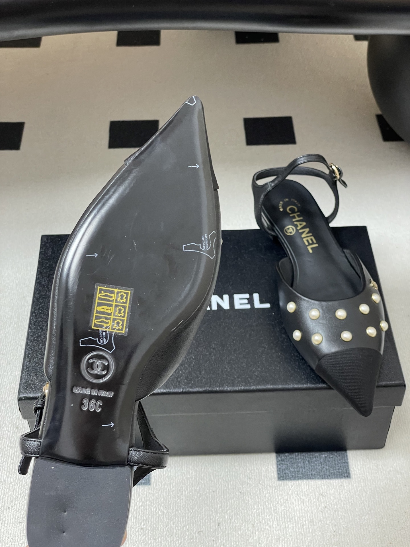 A pair of black Chanel slingback flats with pearl studs, pointed fabric cap toes, and gold CC logo on a black surface. - Hình 8