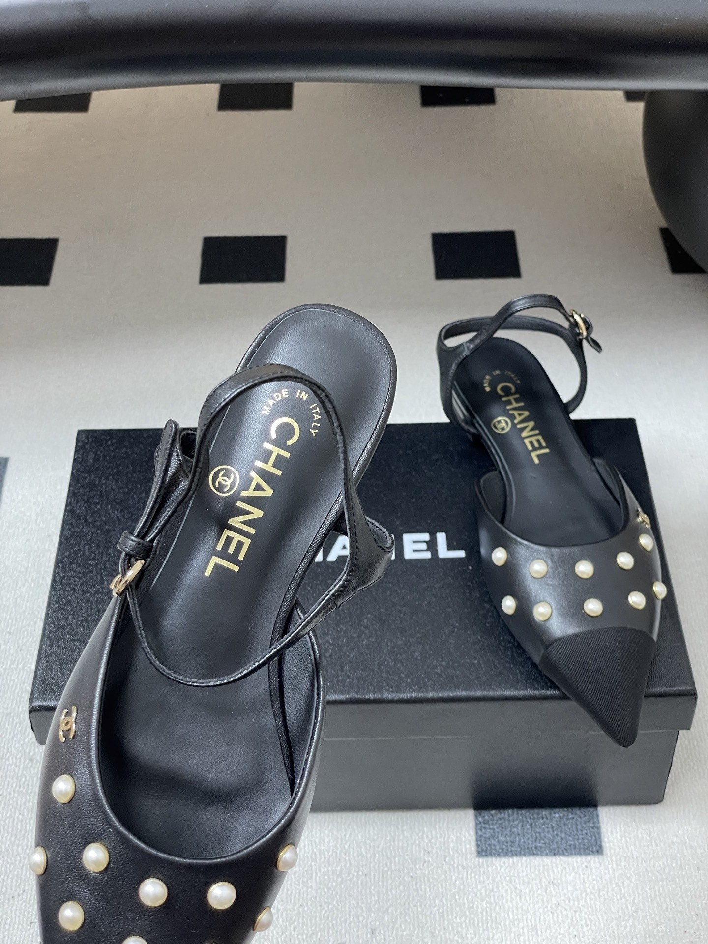 A pair of black Chanel slingback flats with pearl studs, pointed fabric cap toes, and gold CC logo on a black surface. - Hình 7