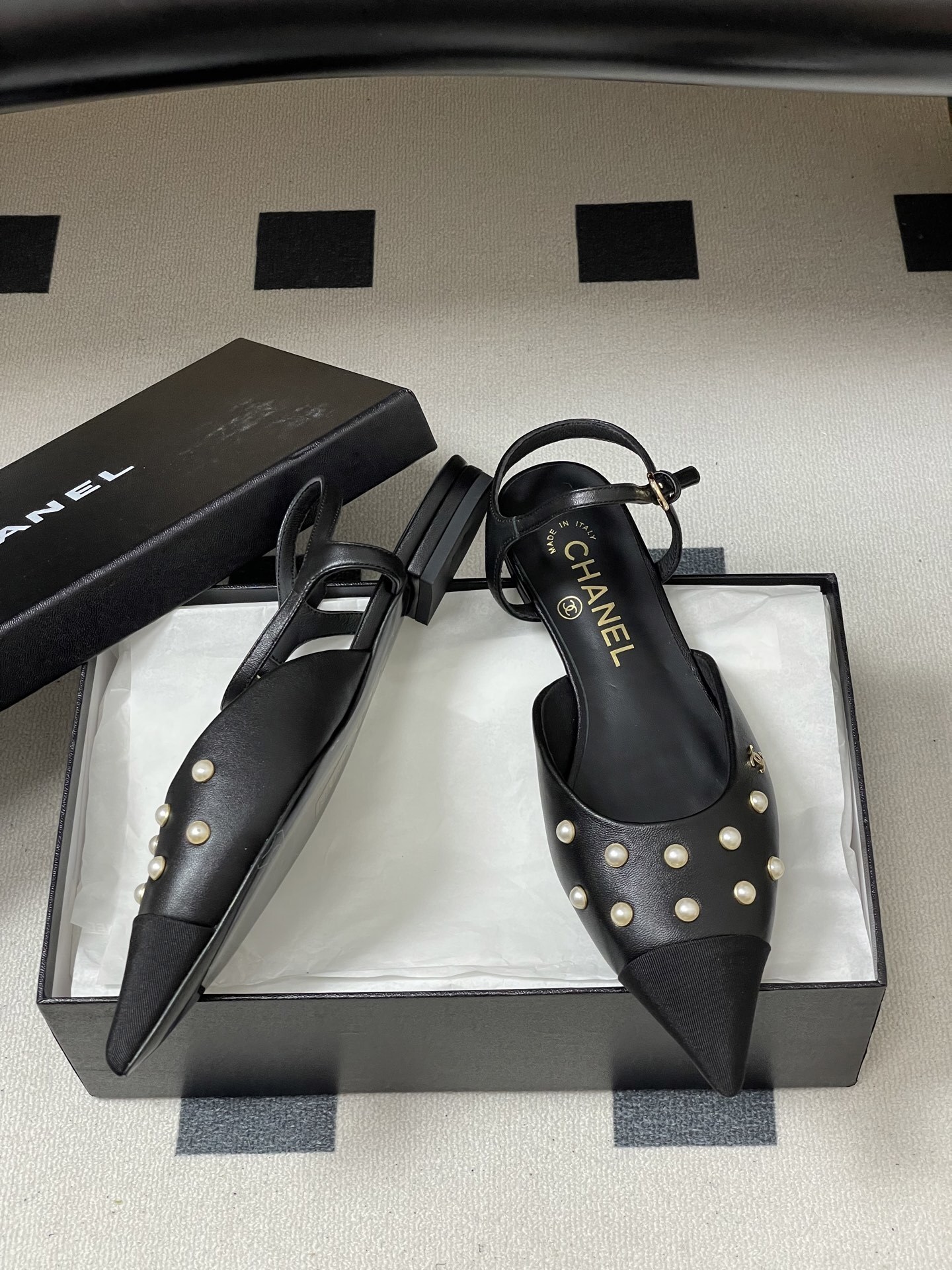 A pair of black Chanel slingback flats with pearl studs, pointed fabric cap toes, and gold CC logo on a black surface. - Hình 6