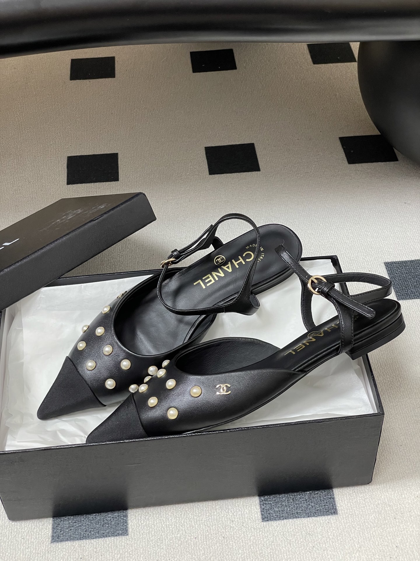 A pair of black Chanel slingback flats with pearl studs, pointed fabric cap toes, and gold CC logo on a black surface. - Hình 4