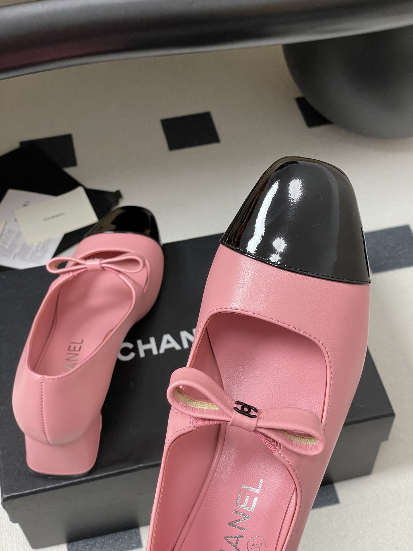 A pair of Chanel pink leather Mary Jane shoes with black patent toe caps and CC logo bows on a black surface - Hình 9