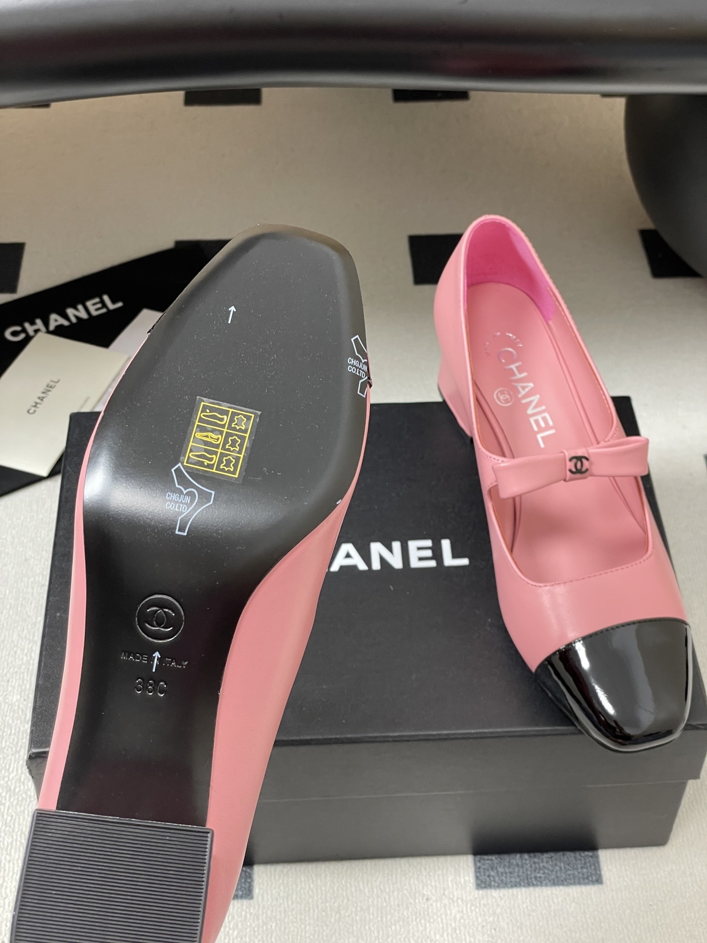 A pair of Chanel pink leather Mary Jane shoes with black patent toe caps and CC logo bows on a black surface - Hình 8