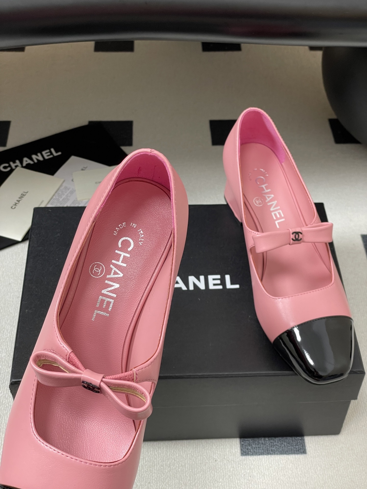 A pair of Chanel pink leather Mary Jane shoes with black patent toe caps and CC logo bows on a black surface - Hình 7
