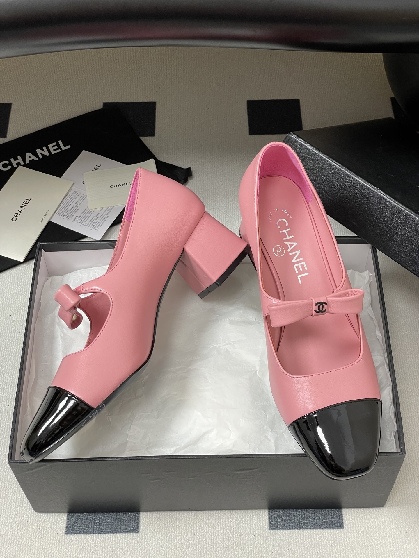 A pair of Chanel pink leather Mary Jane shoes with black patent toe caps and CC logo bows on a black surface - Hình 6