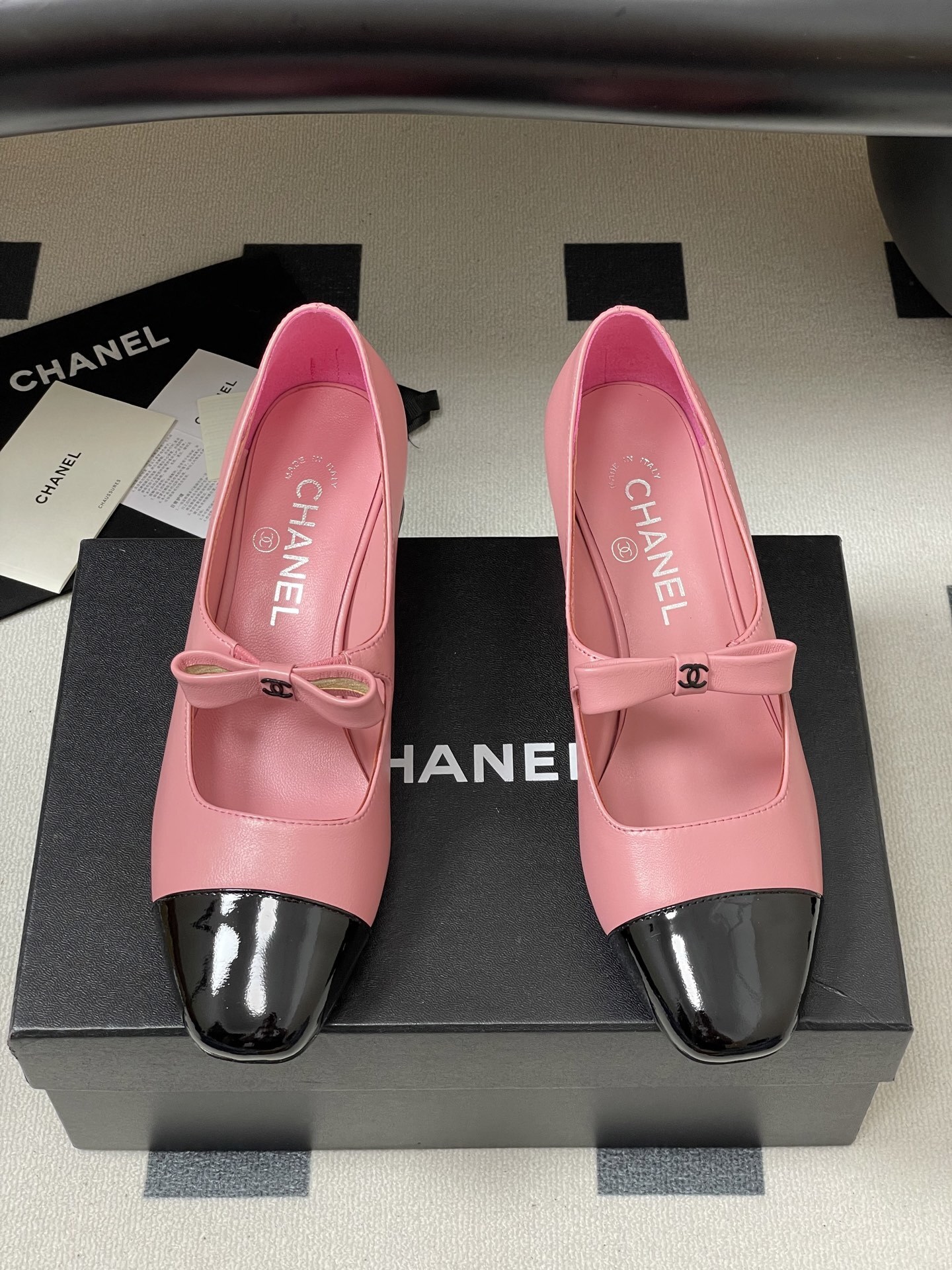 A pair of Chanel pink leather Mary Jane shoes with black patent toe caps and CC logo bows on a black surface - Hình 5