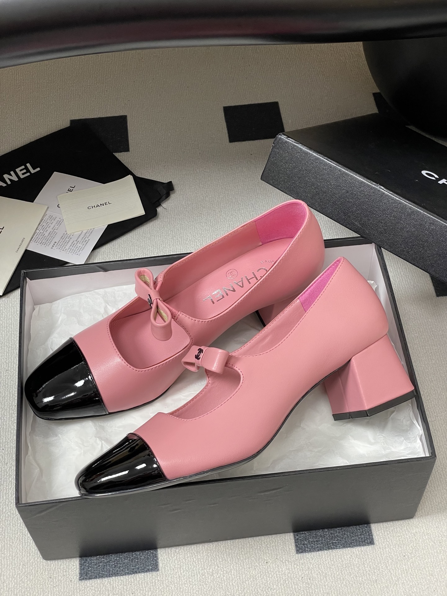 A pair of Chanel pink leather Mary Jane shoes with black patent toe caps and CC logo bows on a black surface - Hình 4