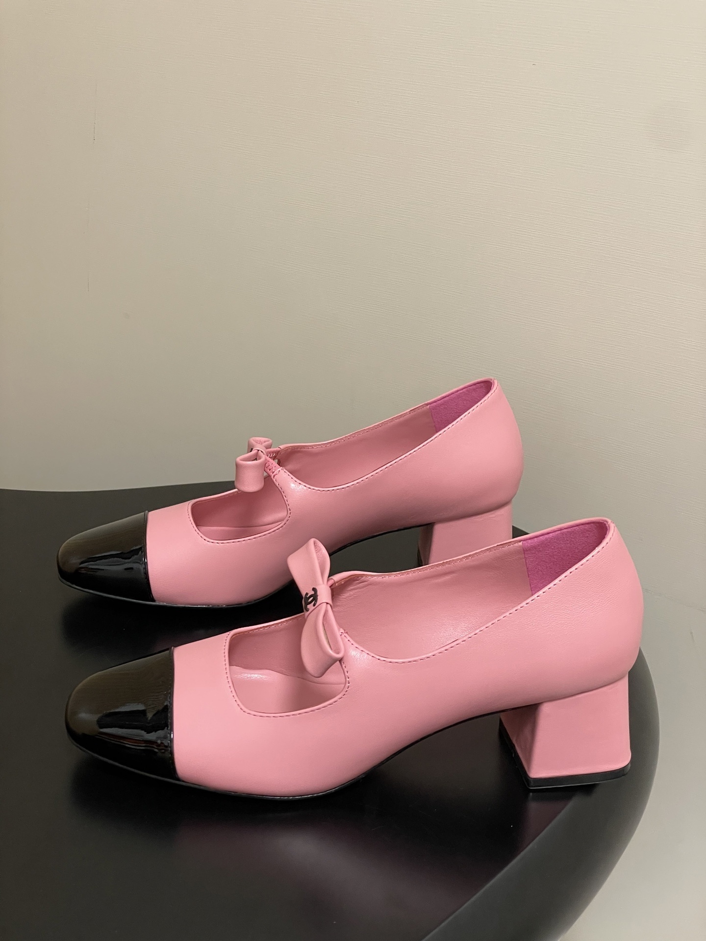 A pair of Chanel pink leather Mary Jane shoes with black patent toe caps and CC logo bows on a black surface - Hình 3