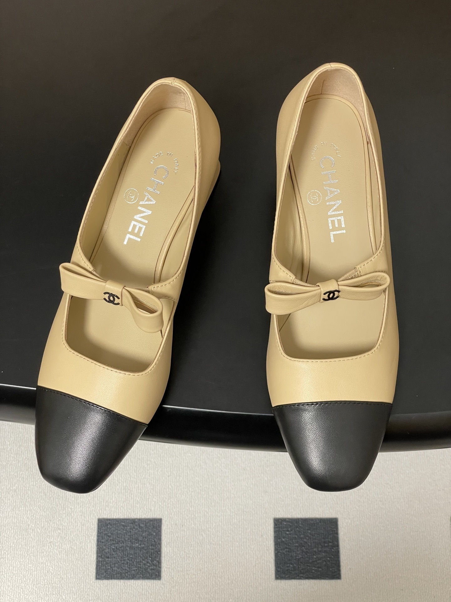 A pair of luxury Chanel beige leather Mary Jane pumps with black toe caps and CC logo bow details. - Hình 2