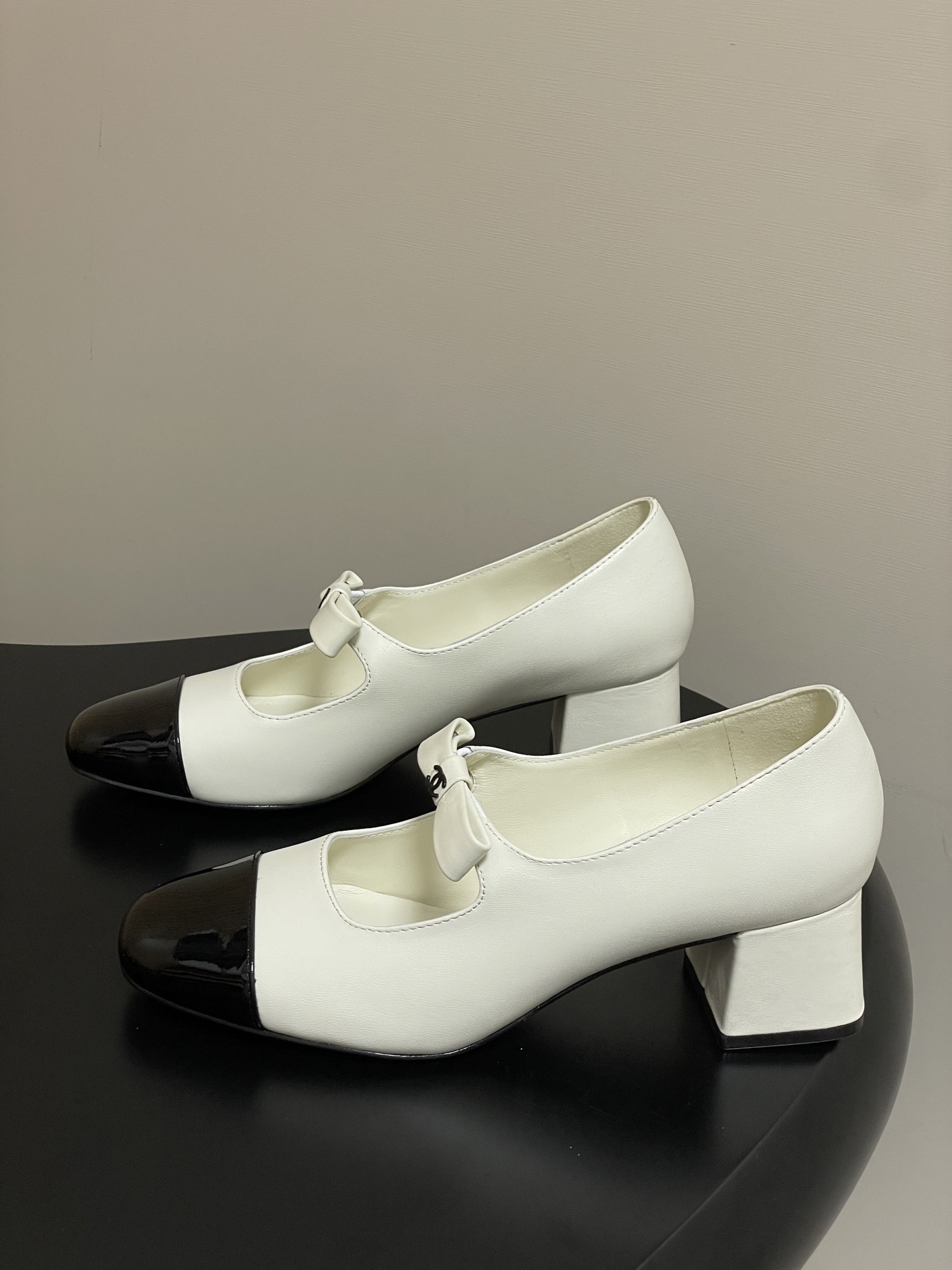 A pair of white leather Mary Jane block heels with black patent leather cap toes and decorative bows. - Hình 3