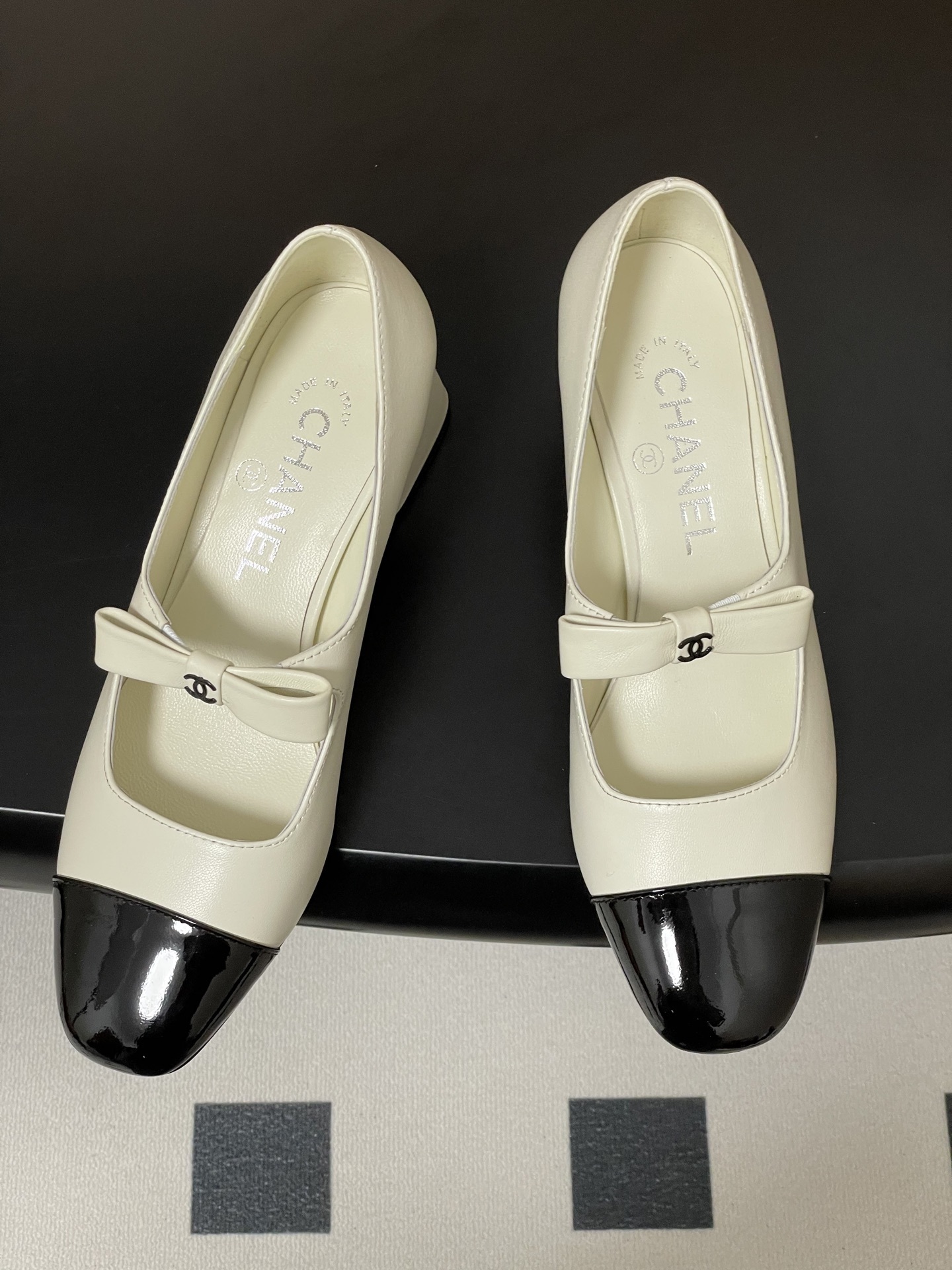 A pair of white leather Mary Jane block heels with black patent leather cap toes and decorative bows. - Hình 2