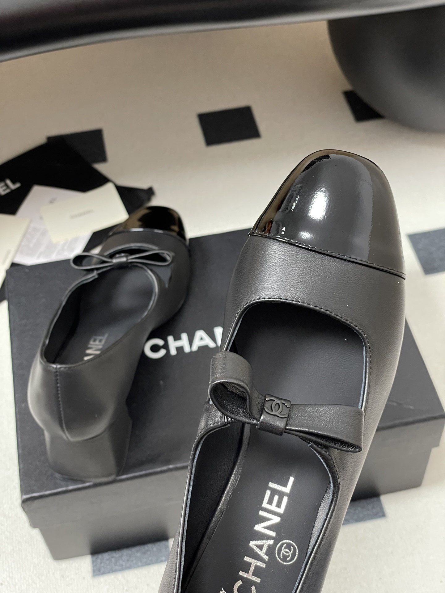 A pair of elegant black Chanel Mary Jane pumps with patent leather cap toes and bow accents featuring the CC logo. - Hình 9