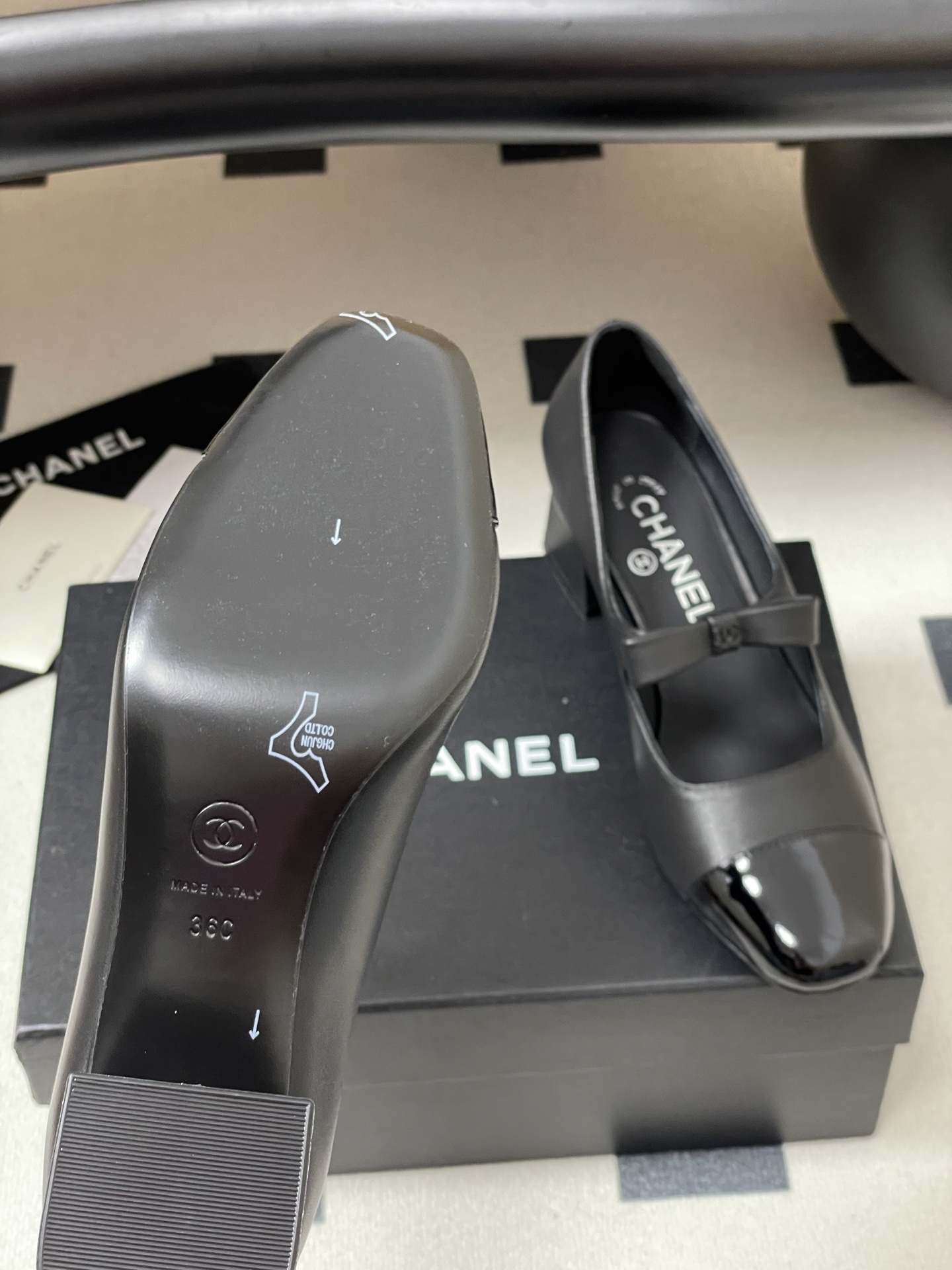 A pair of elegant black Chanel Mary Jane pumps with patent leather cap toes and bow accents featuring the CC logo. - Hình 8