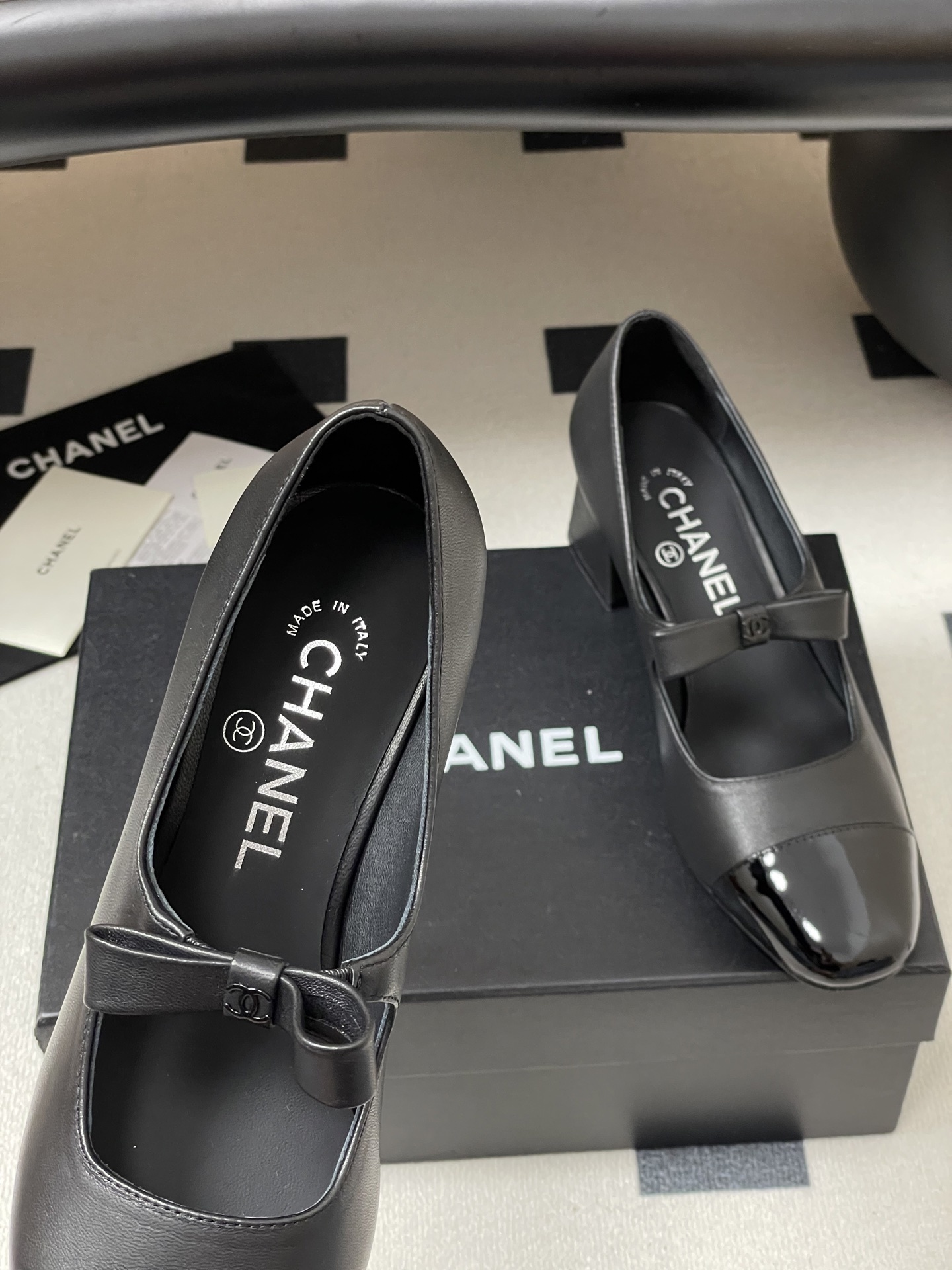 A pair of elegant black Chanel Mary Jane pumps with patent leather cap toes and bow accents featuring the CC logo. - Hình 7