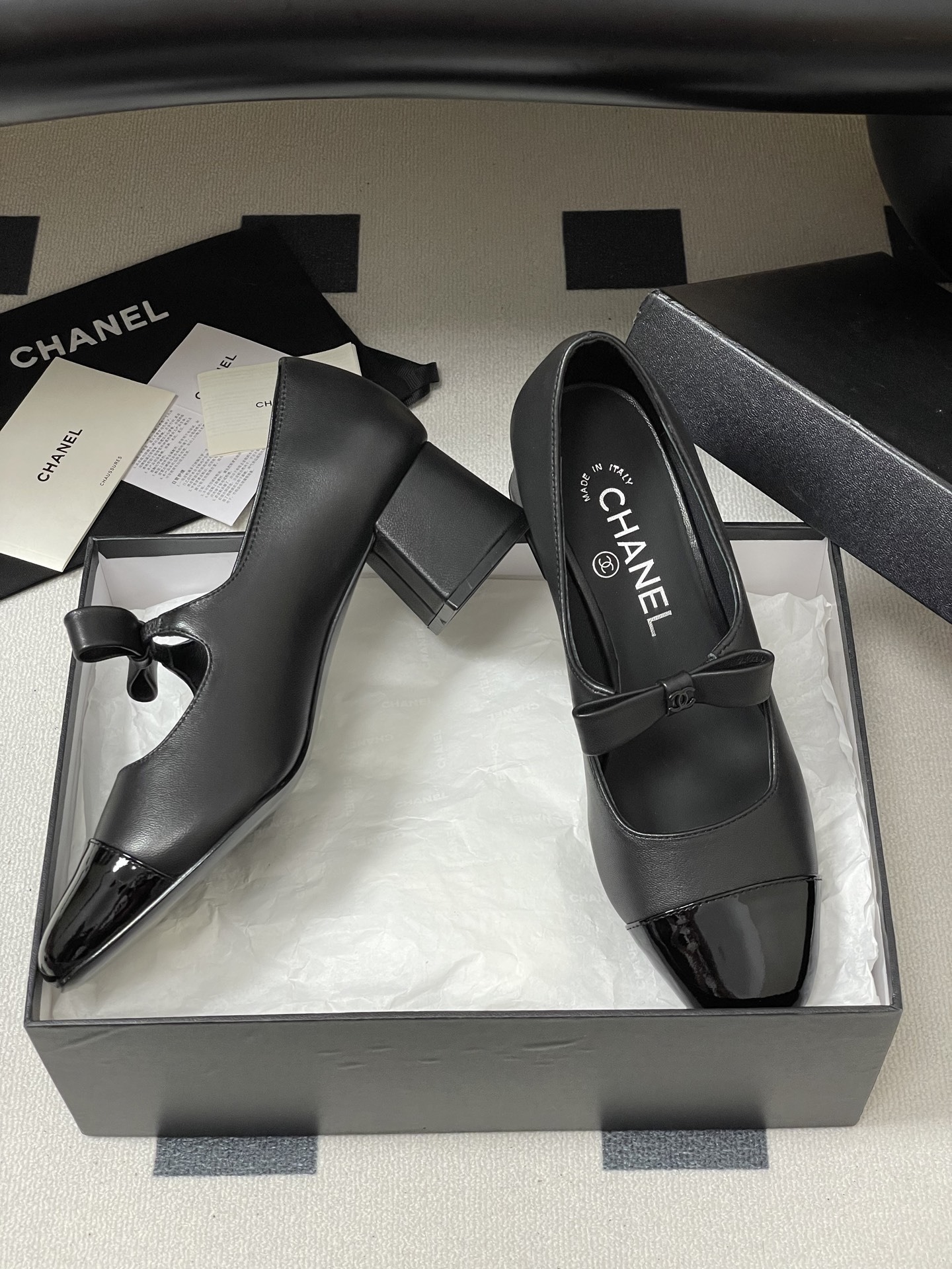 A pair of elegant black Chanel Mary Jane pumps with patent leather cap toes and bow accents featuring the CC logo. - Hình 6