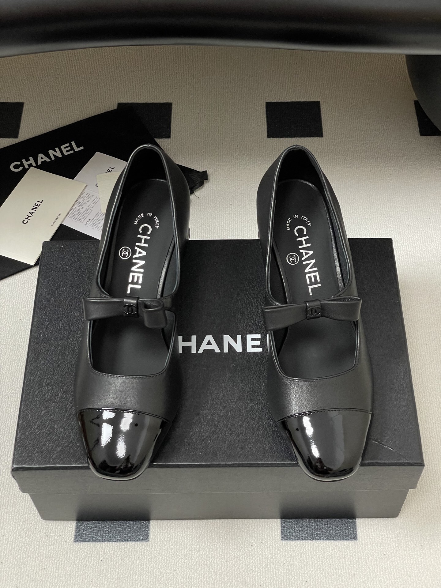 A pair of elegant black Chanel Mary Jane pumps with patent leather cap toes and bow accents featuring the CC logo. - Hình 5