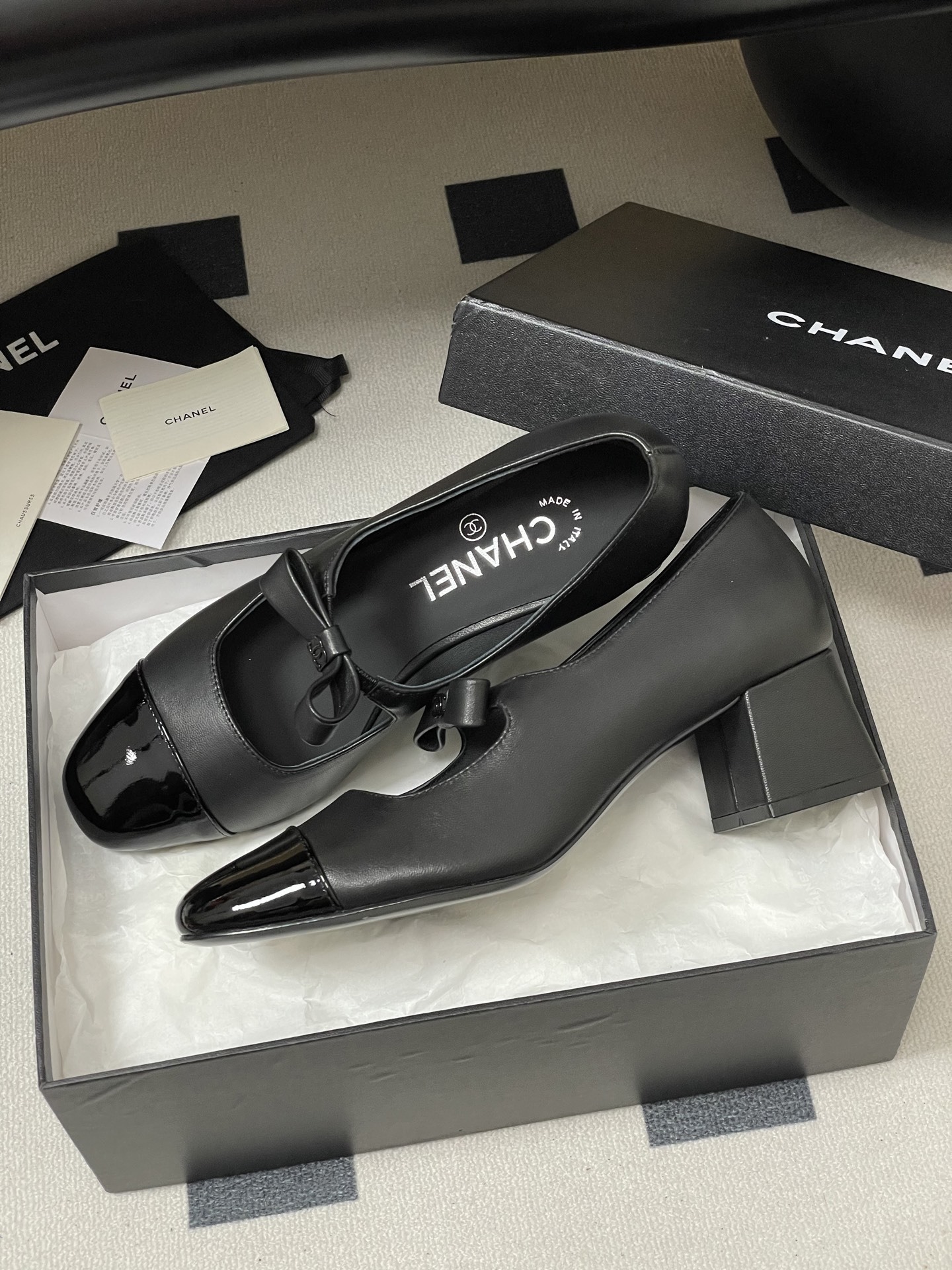 A pair of elegant black Chanel Mary Jane pumps with patent leather cap toes and bow accents featuring the CC logo. - Hình 4