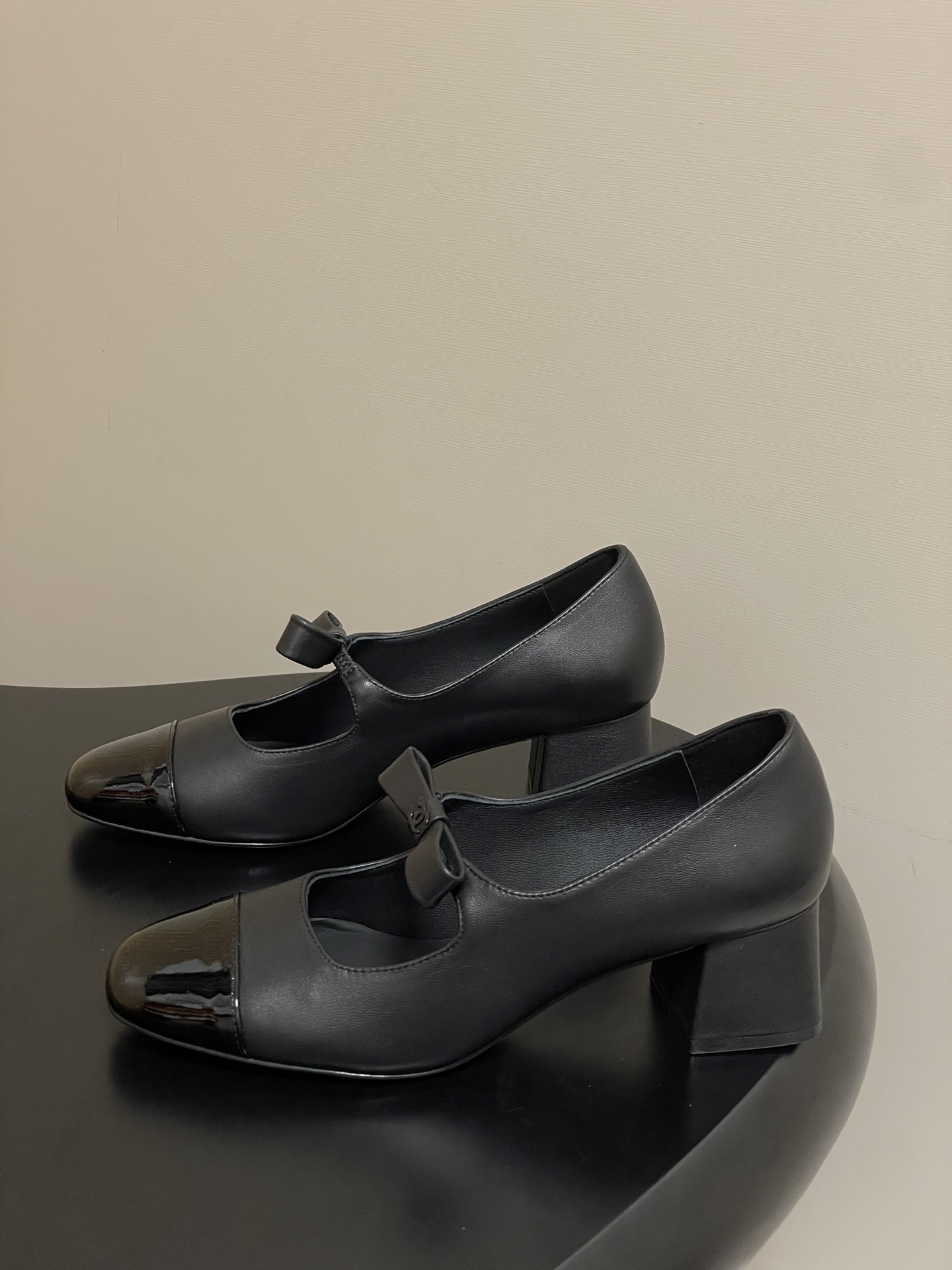A pair of elegant black Chanel Mary Jane pumps with patent leather cap toes and bow accents featuring the CC logo. - Hình 3