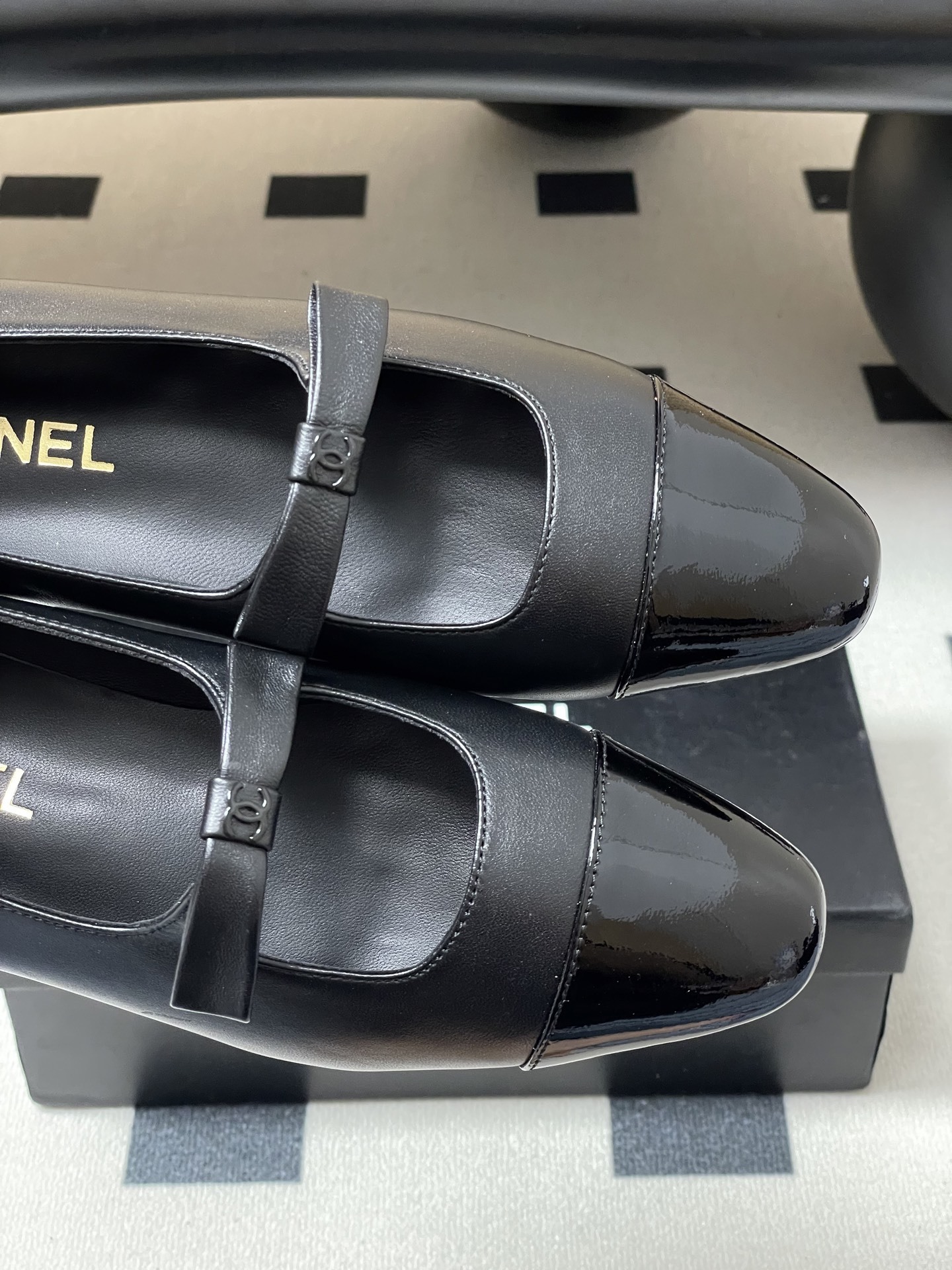 A pair of authentic Chanel black leather Mary Jane flats with glossy patent leather toe caps and CC logo straps displayed on a black surface. - Hình 7