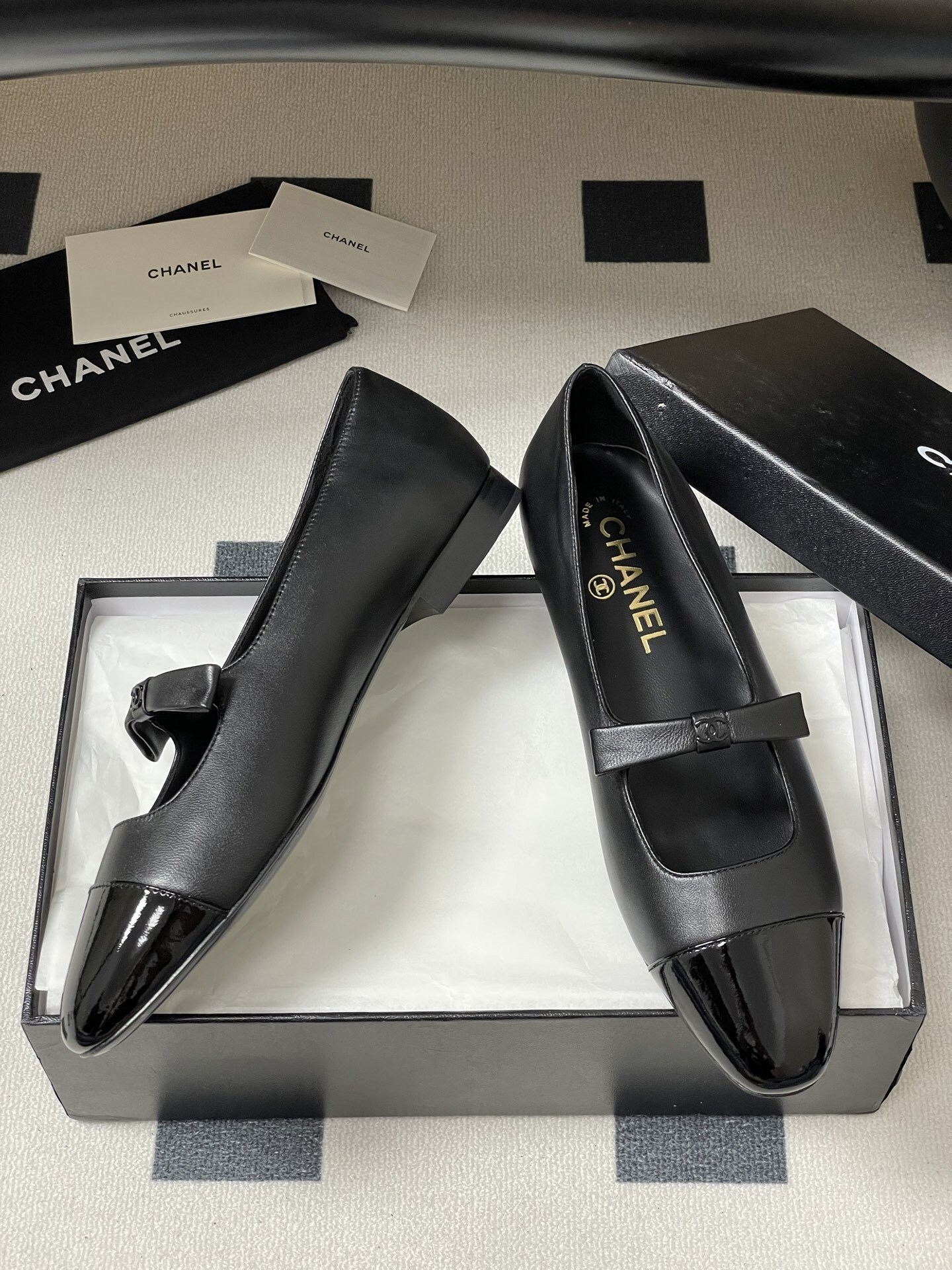 A pair of authentic Chanel black leather Mary Jane flats with glossy patent leather toe caps and CC logo straps displayed on a black surface. - Hình 6