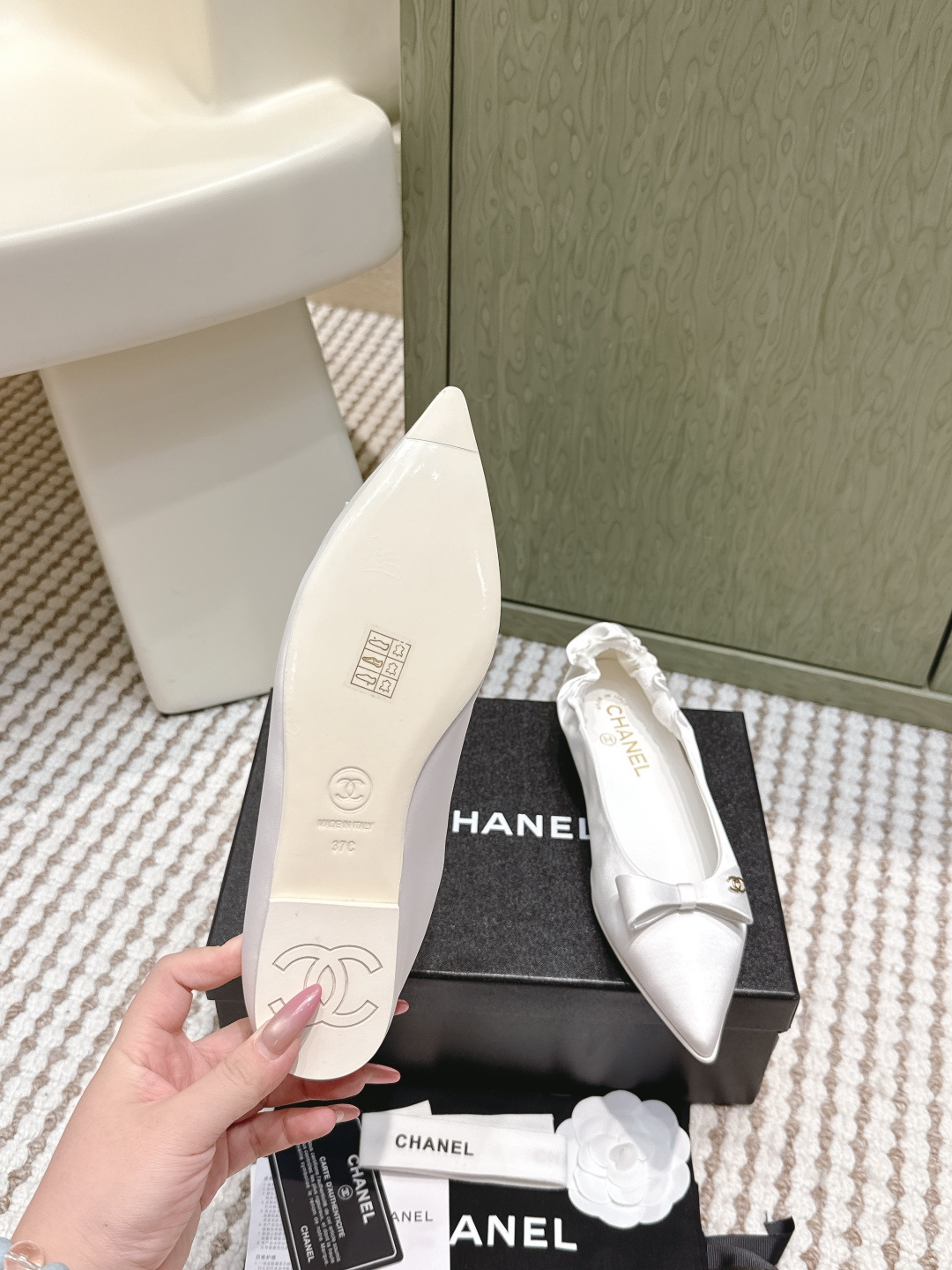 Pair of elegant Chanel white satin pointed-toe ballerina flats with bows and gold logos on a black box. - Hình 9