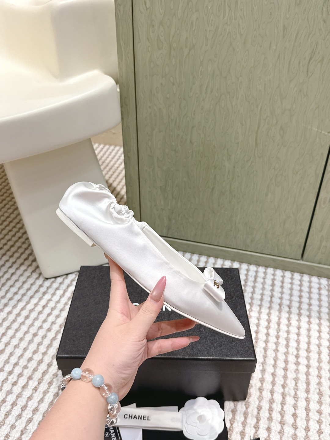 Pair of elegant Chanel white satin pointed-toe ballerina flats with bows and gold logos on a black box. - Hình 5